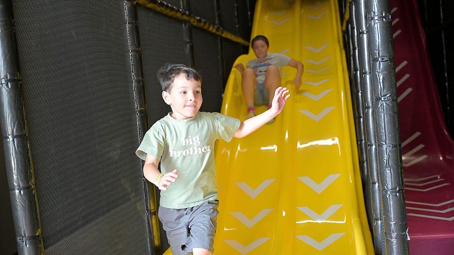Young boy running off a large yellow slide at an indoor play center.