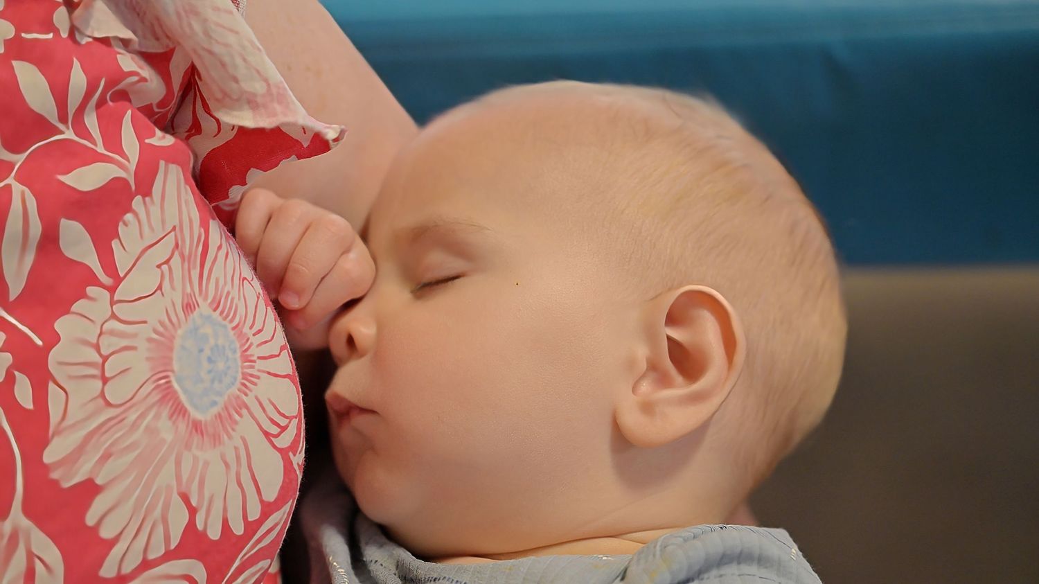 Close-up of a sleeping baby nursing against a floral pink pillow.