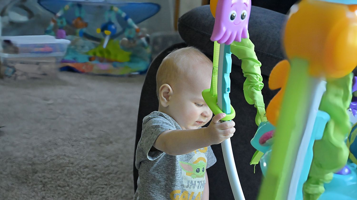 A baby reaches out to touch colorful toys on a baby activity center in a playroom.