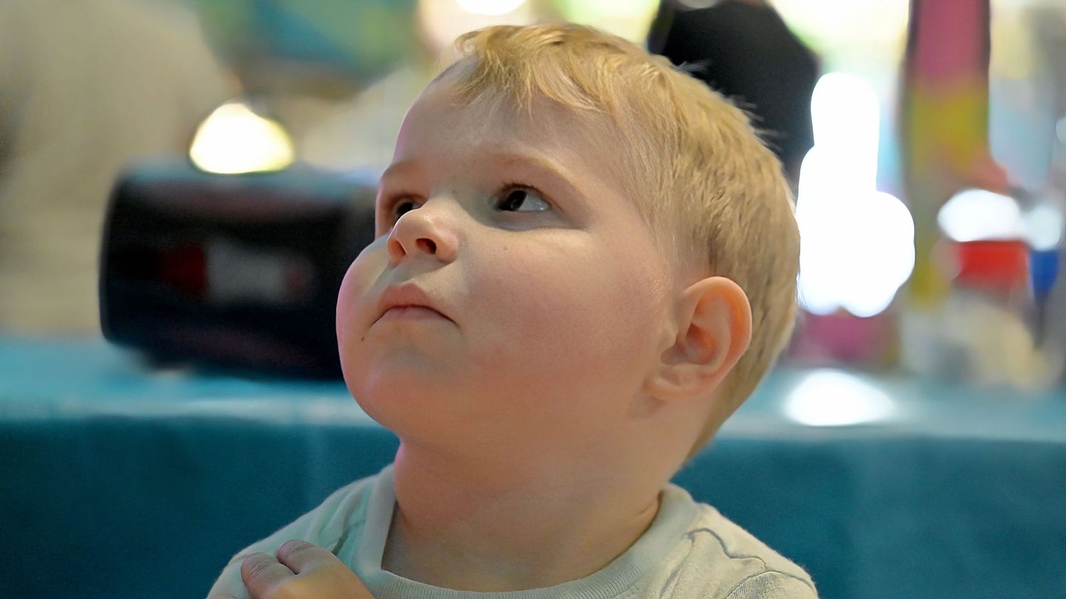 Close-up portrait of a curious toddler with blonde hair looking upward.
