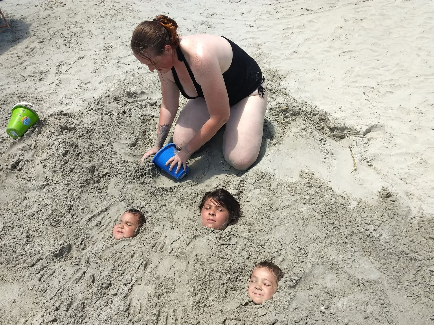A woman burying three children in the sand at the beach.