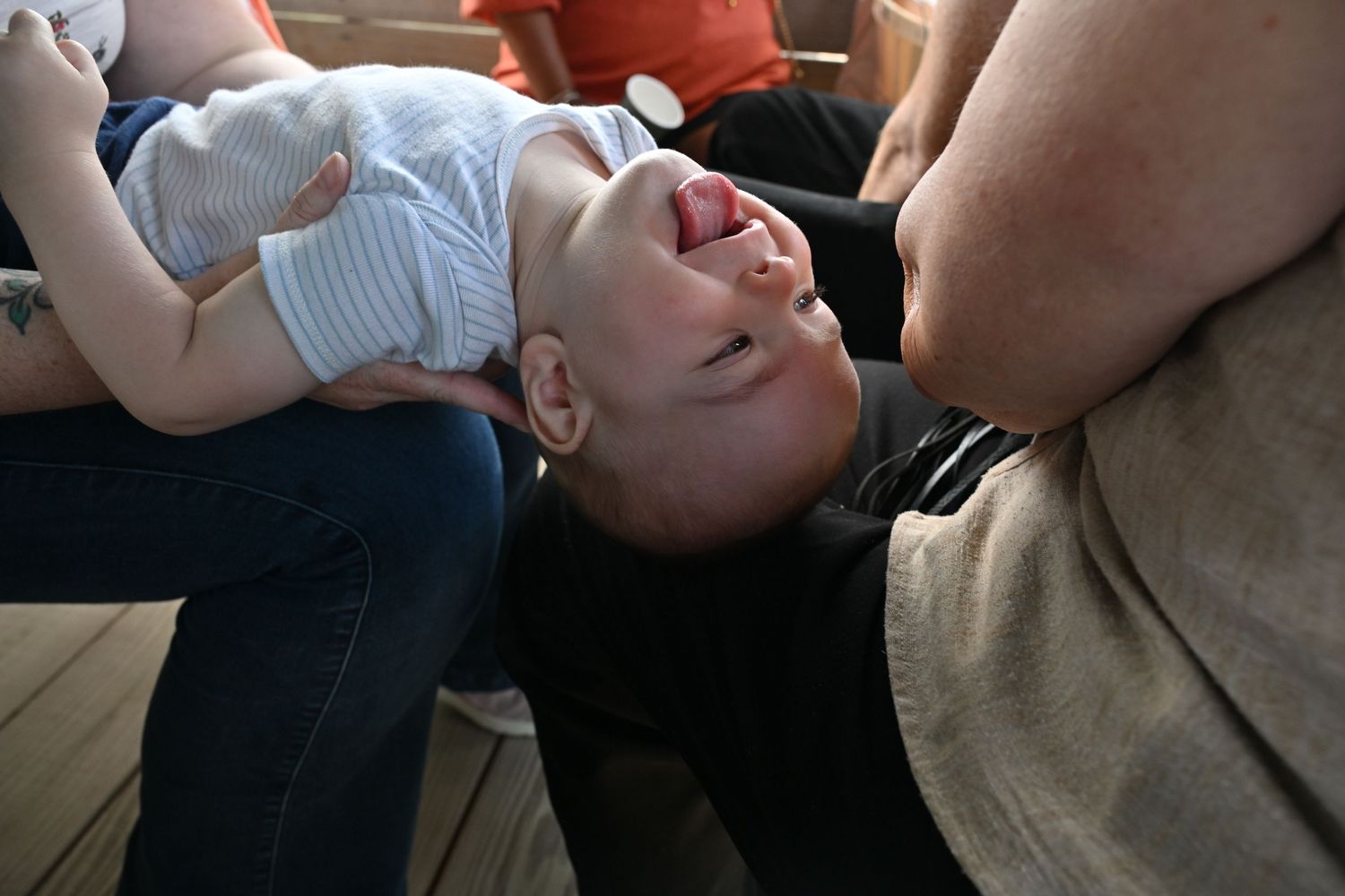 A laughing baby is held upside down by an adult on a wooden deck.