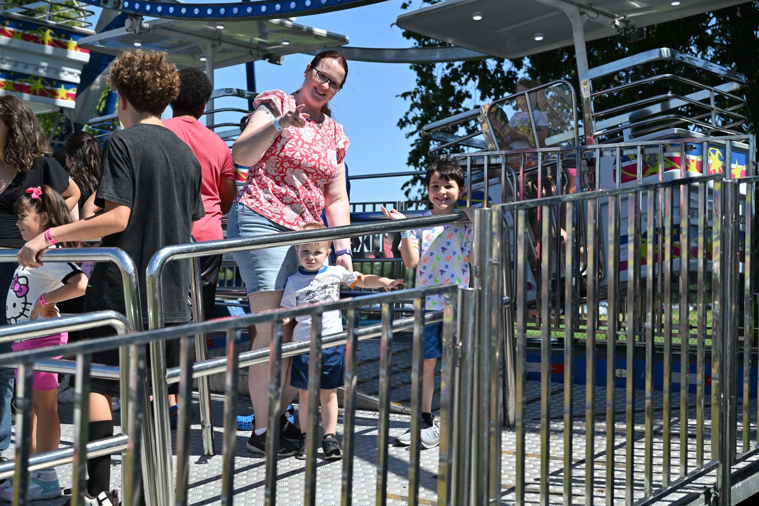 Family waits in line at an outdoor amusement park ride on a sunny day.