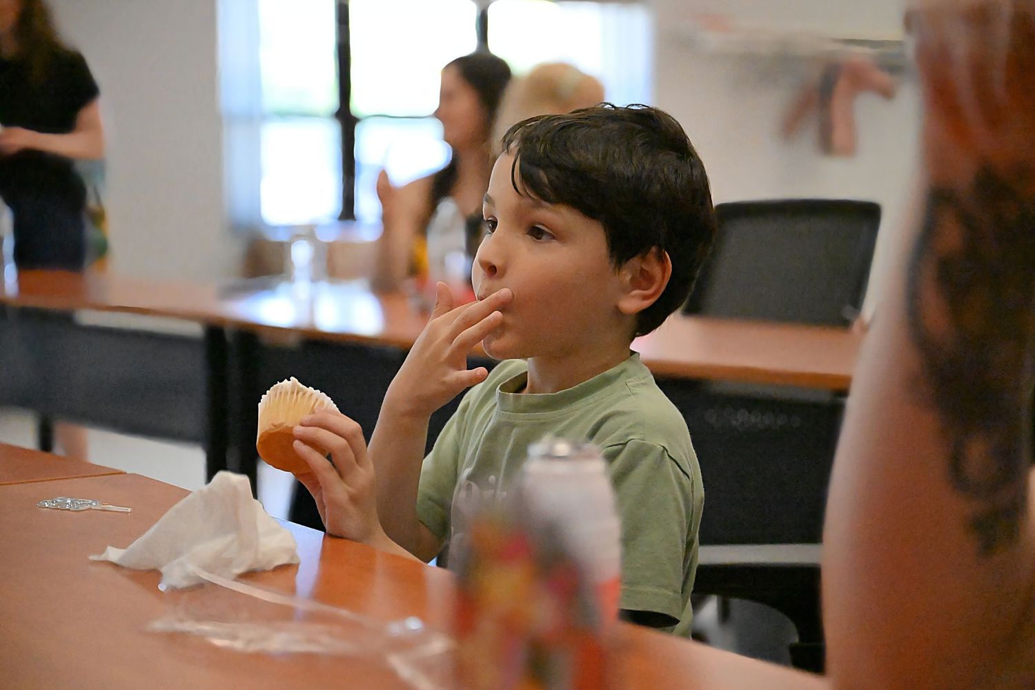 Young boy eating a burger at a table during an indoor event.