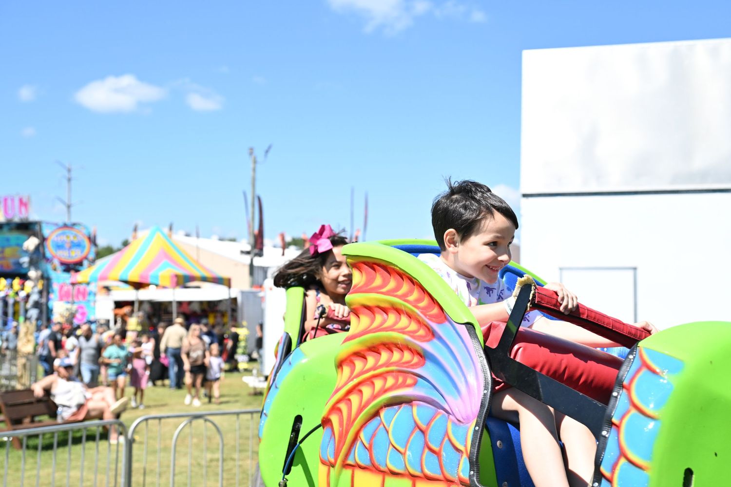 Children enjoy a dragon-themed carnival ride on a sunny day at an outdoor fair.