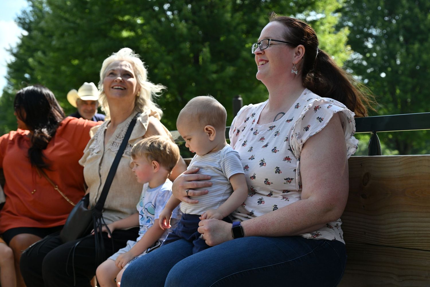 Women and young children sit together on a wagon ride at an outdoor fair.