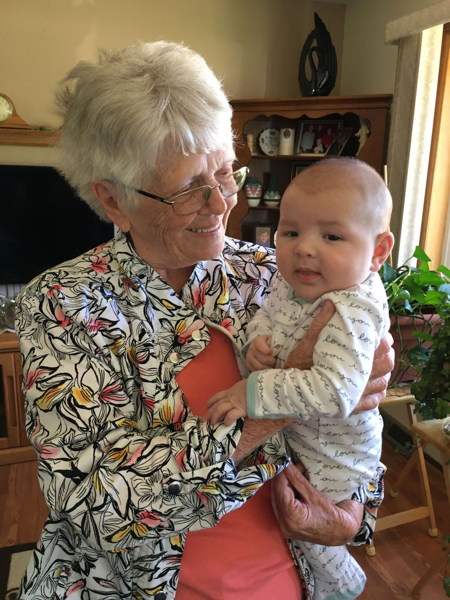 An elderly grandmother smiling while holding a happy baby indoors.