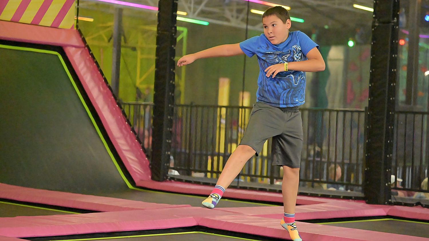 Preteen boy jumping on a trampoline at a colorful indoor trampoline park.