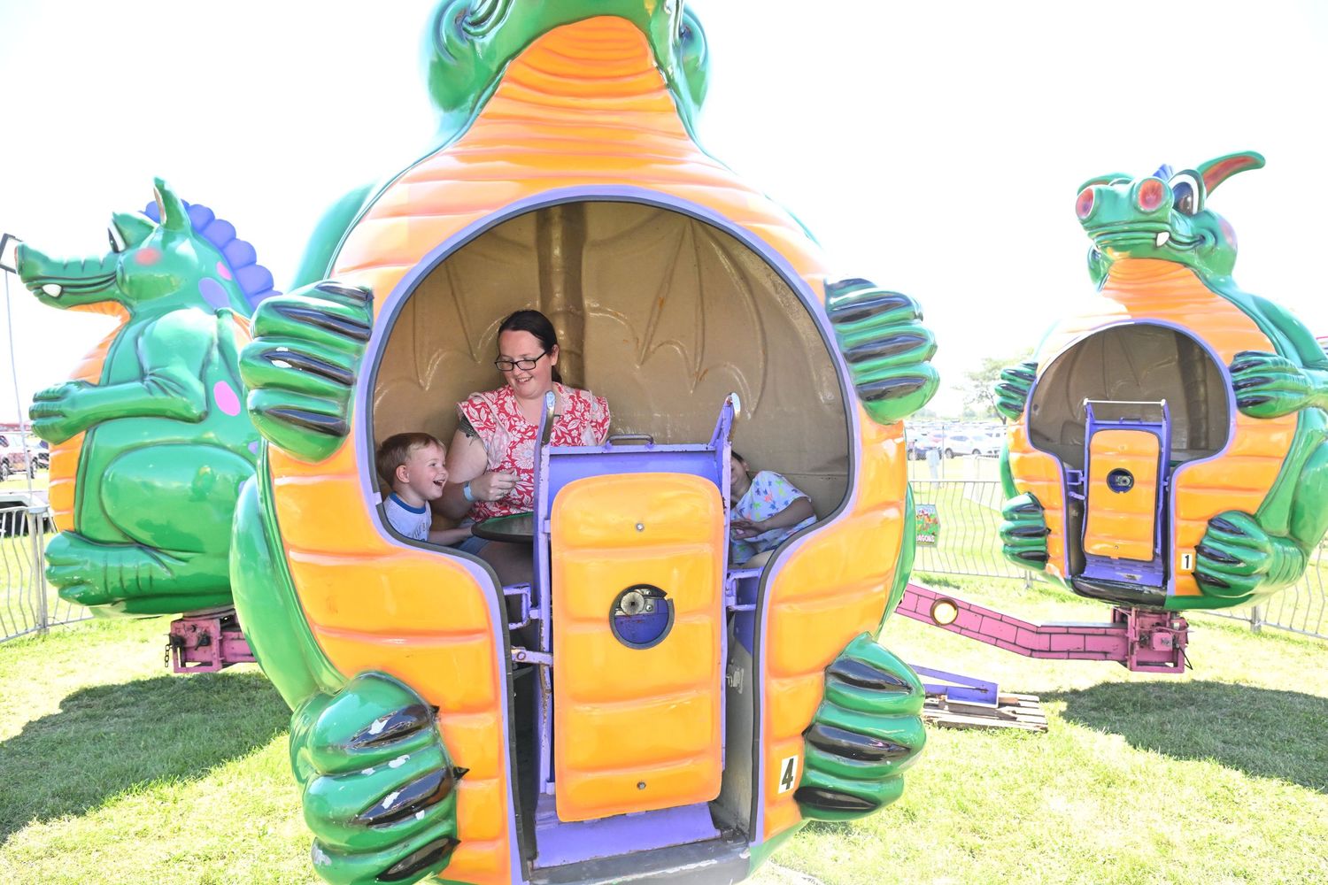 Mother and baby enjoy a dragon-themed inflatable ride at an outdoor carnival.