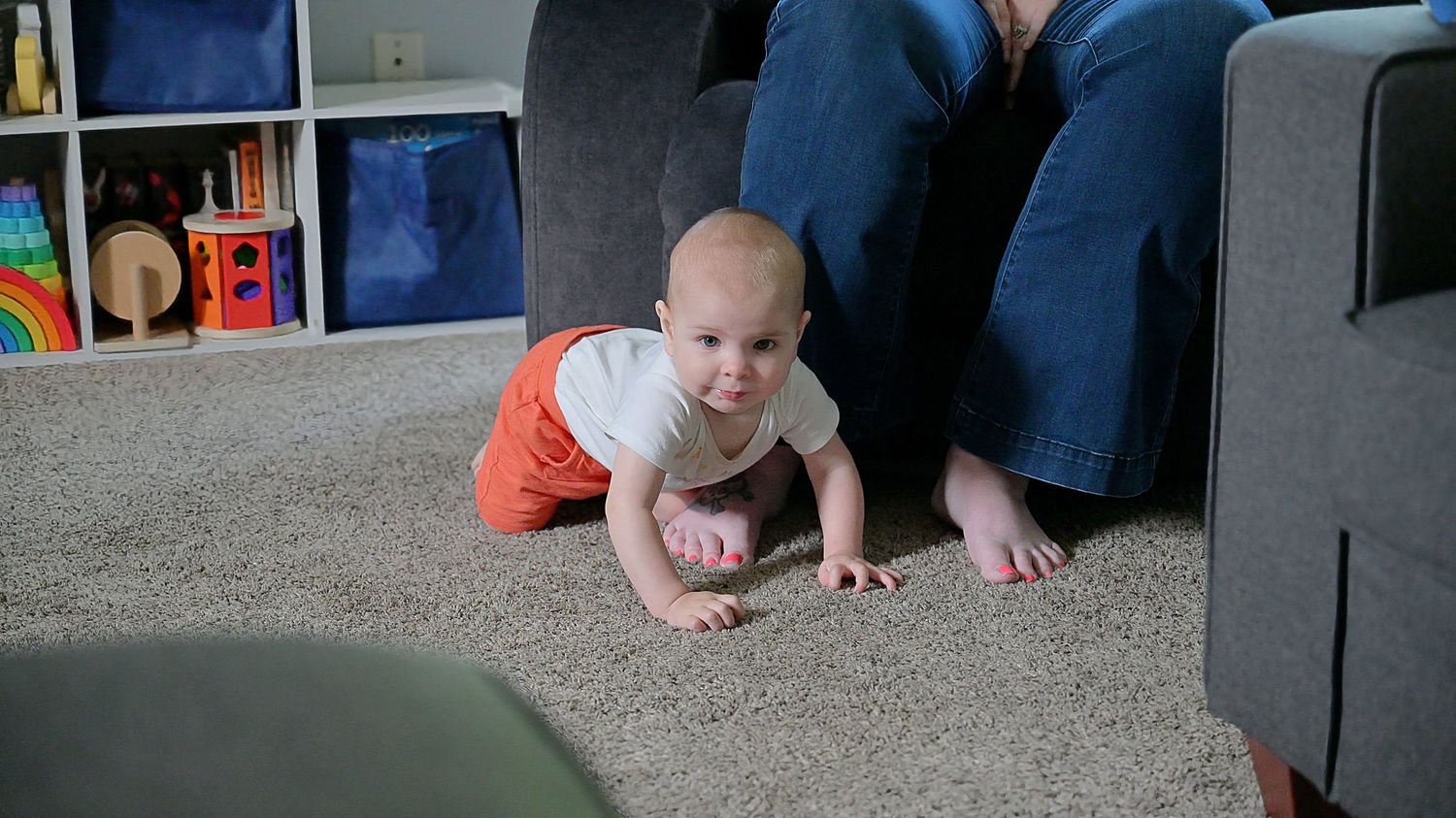 Baby crawling on carpet near couch in playroom.