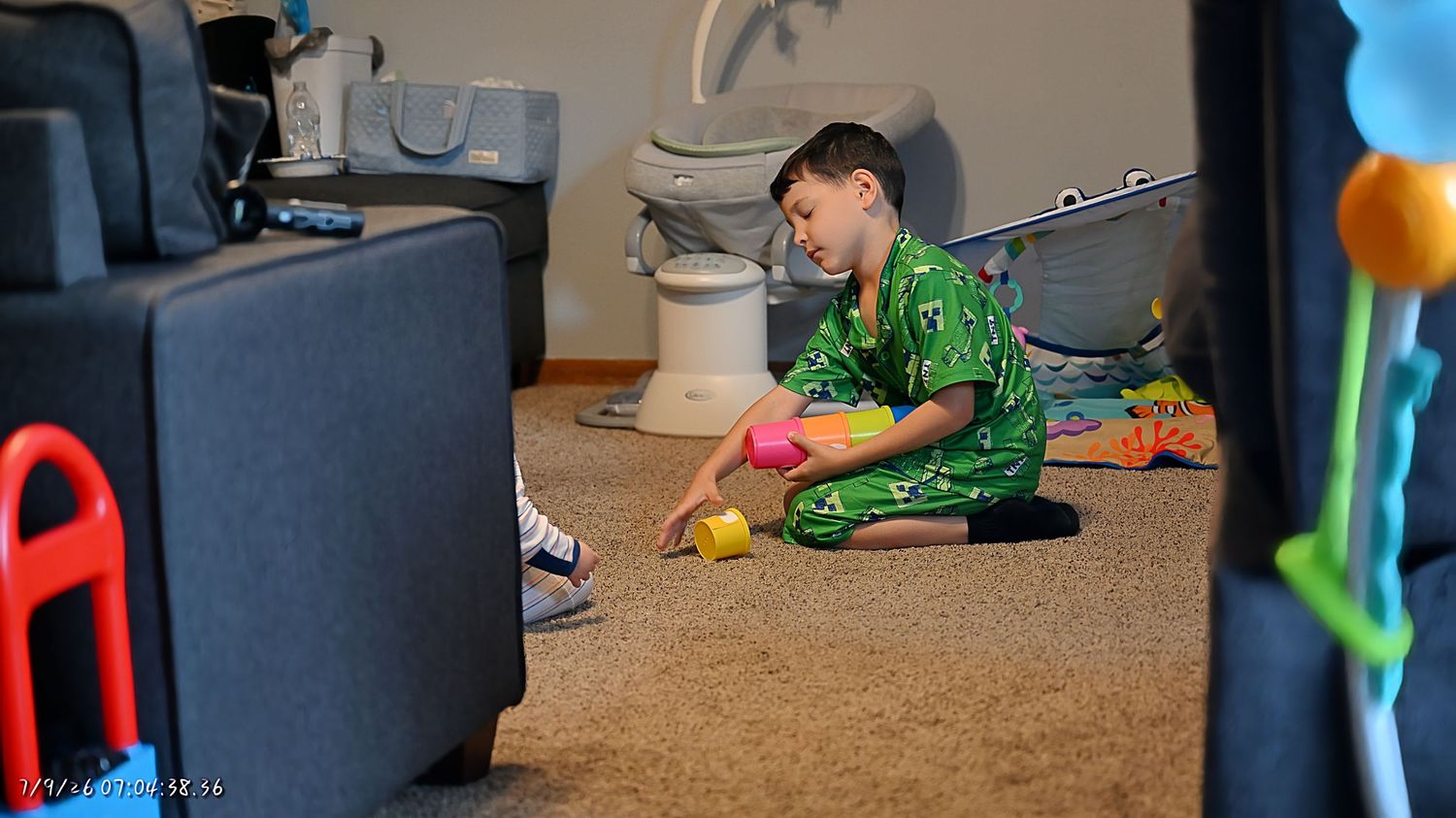 A young boy in green pajamas sitting on carpet playing with colorful toys in a living room.