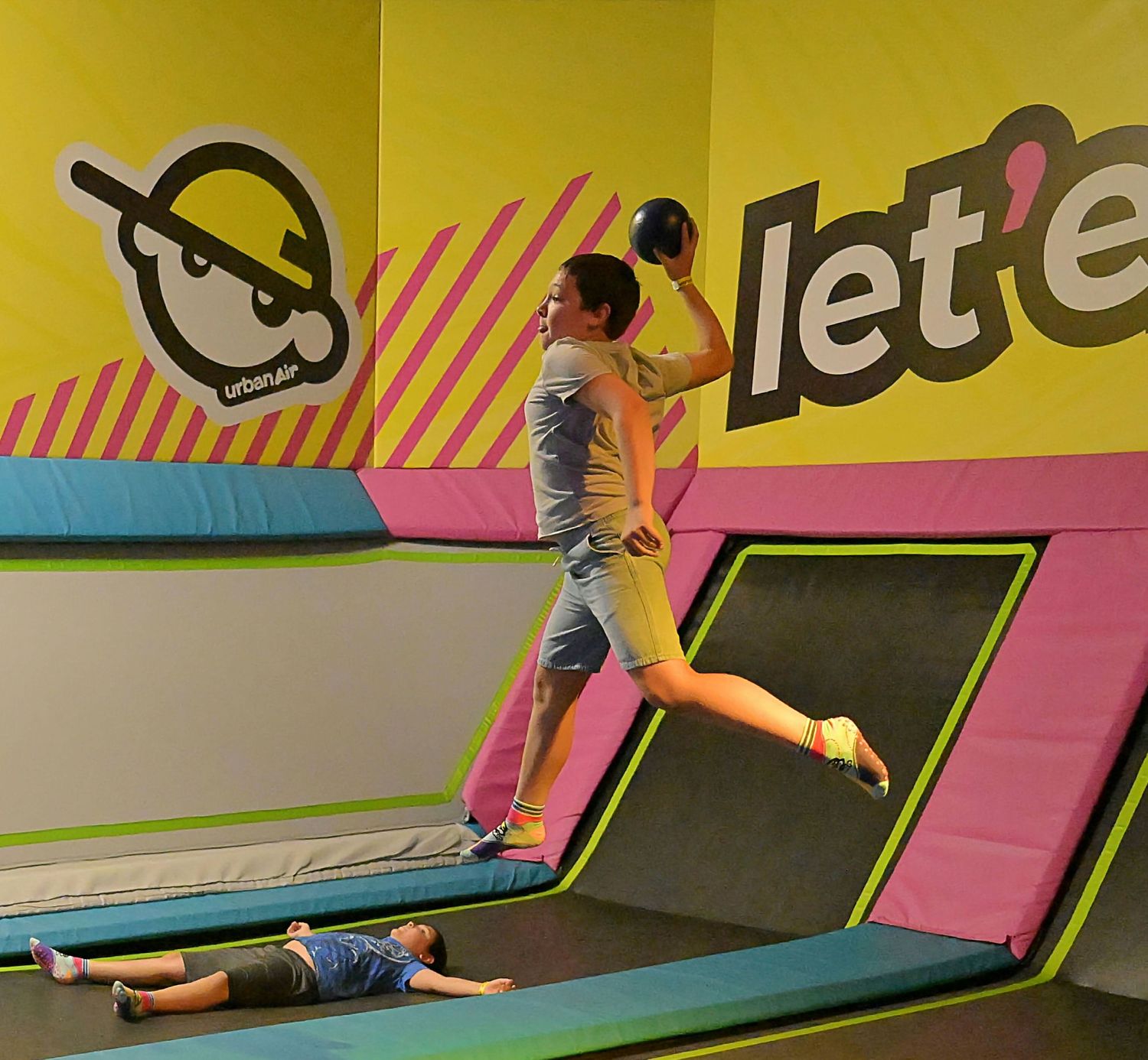 A person jumps high on a trampoline at a colorful indoor trampoline park with Let E signage.