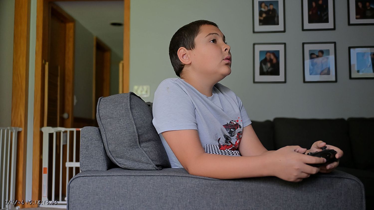 Young boy sitting on a couch playing video games with a controller in a home living room.