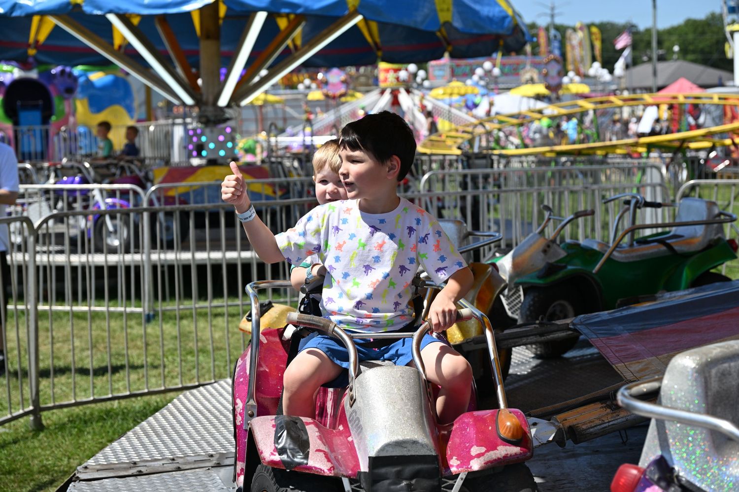 Young boy riding a carnival car ride solo at a colorful outdoor fairground.