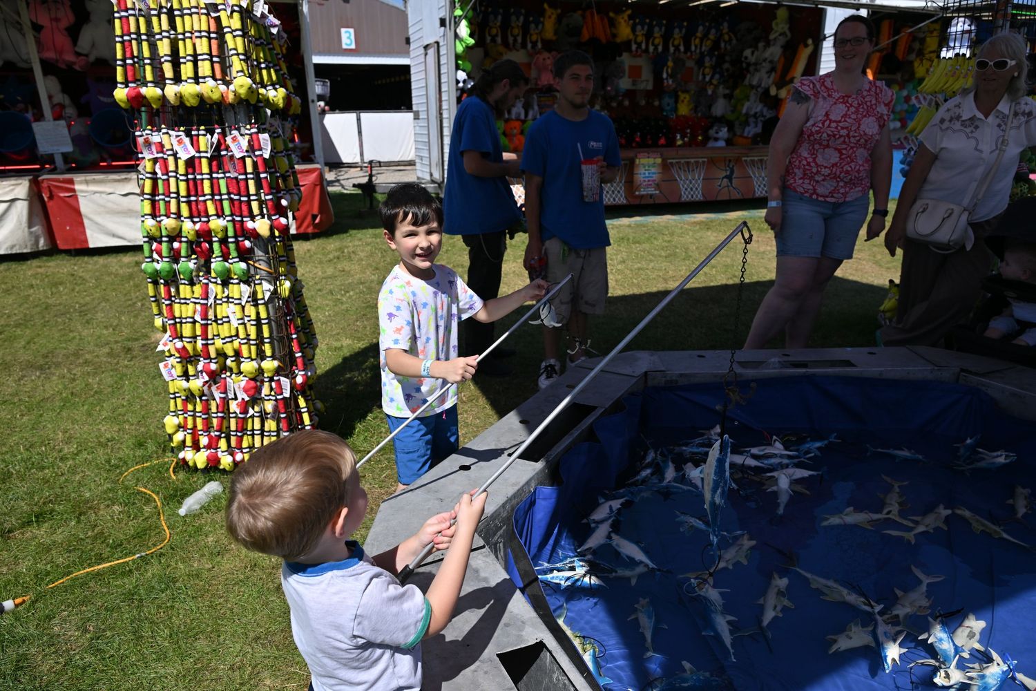 Children play a fishing carnival game with prizes at an outdoor summer fair.