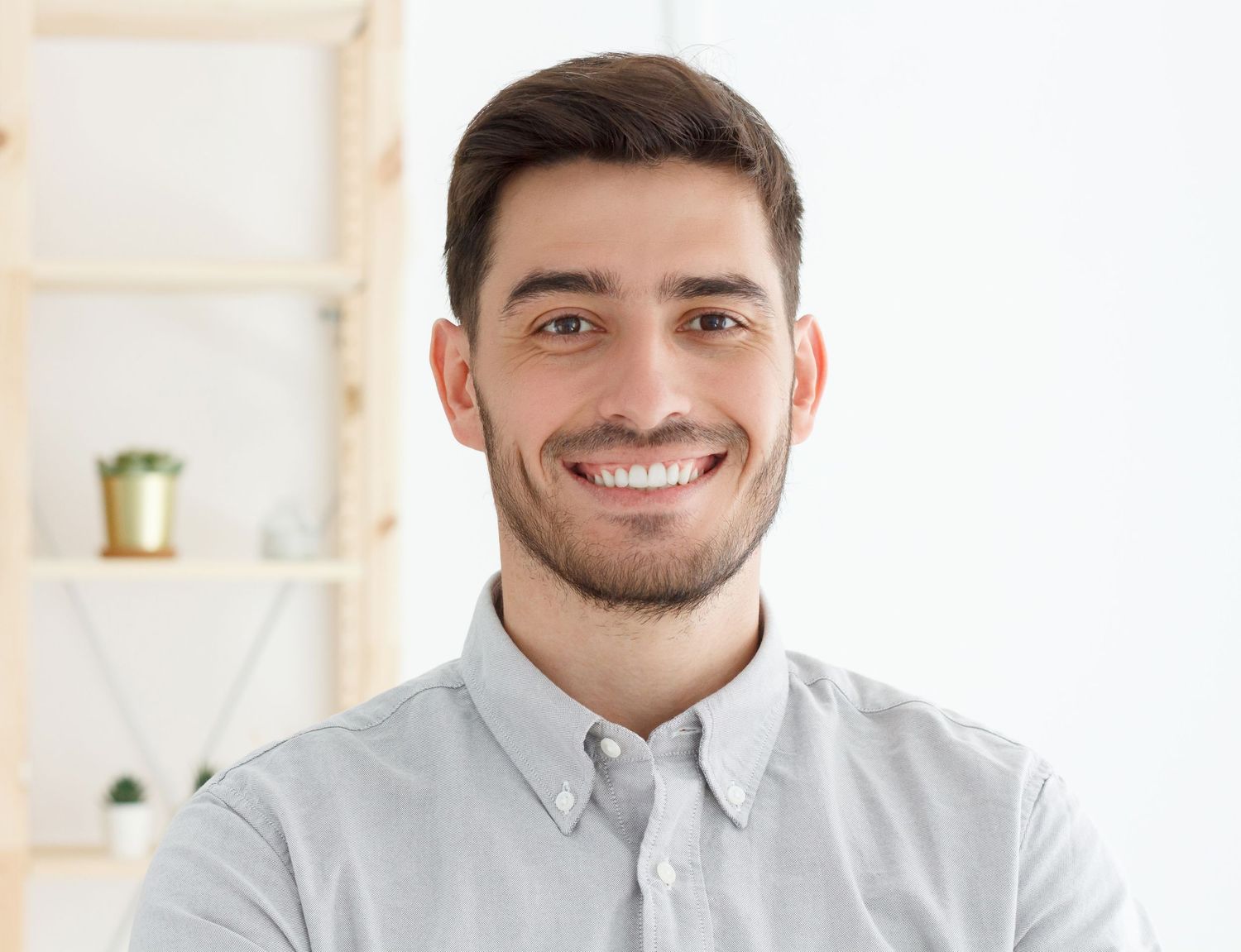 Young smiling man in a light blue shirt standing in a bright modern office space.