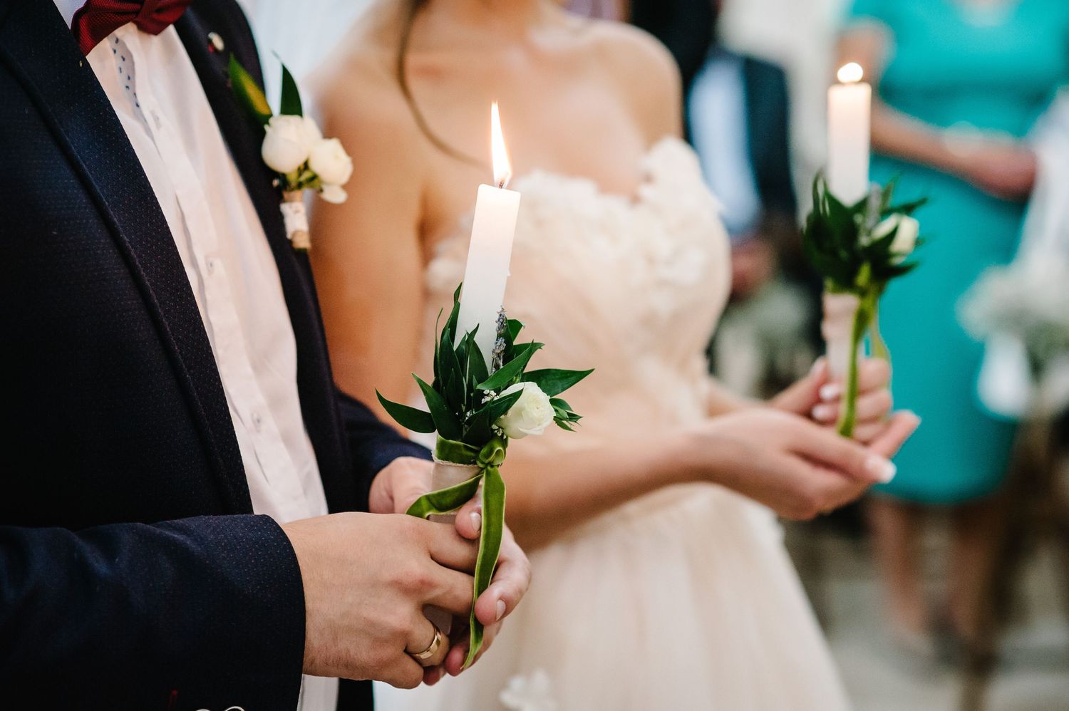 Bride and groom holding lit white candles with greenery during a wedding ceremony.