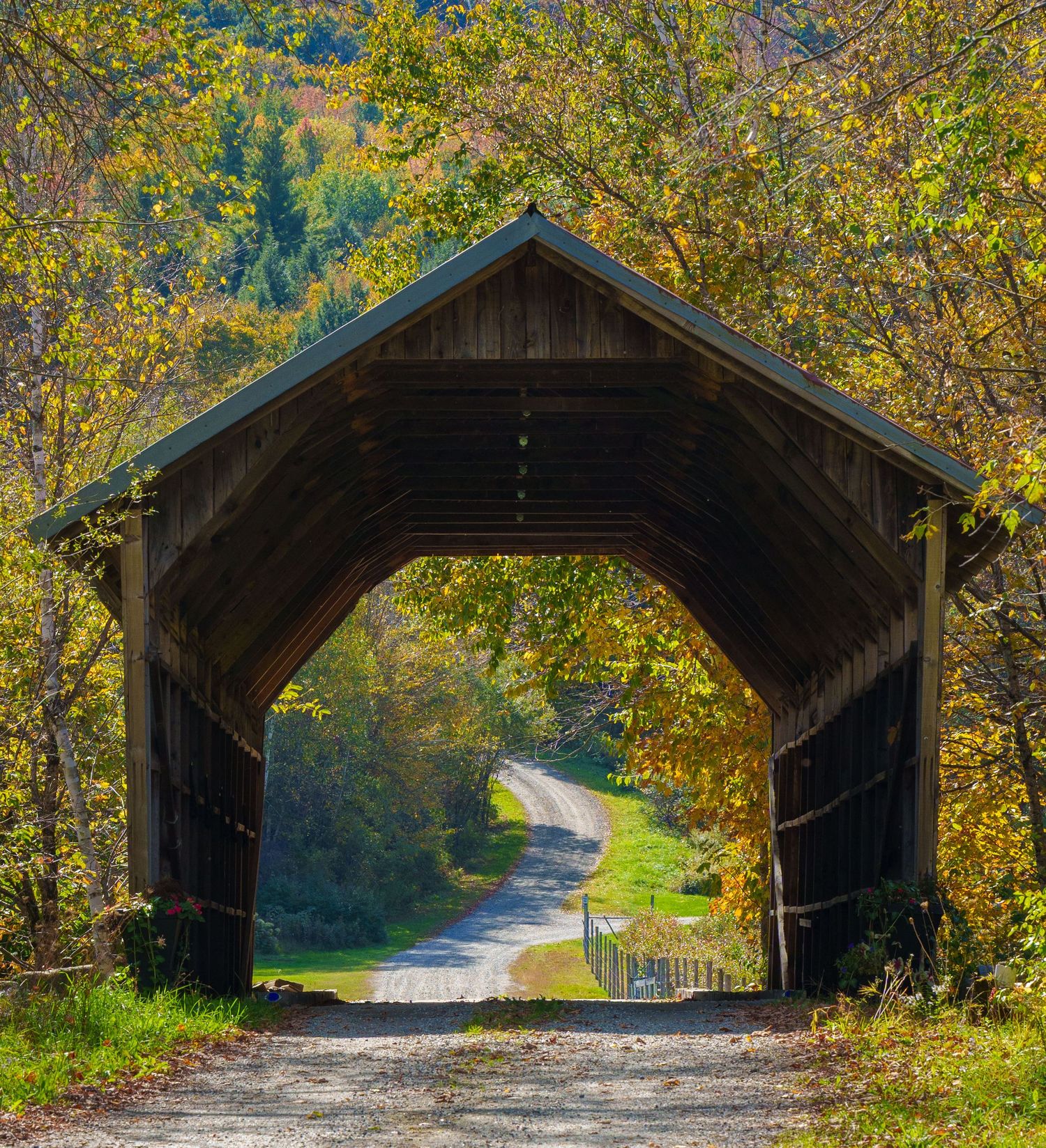 Classic New England covered wooden bridge framing a winding country road surrounded by autumn foliage trees.
