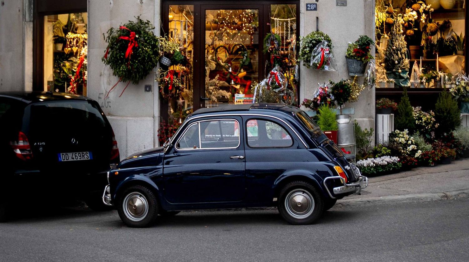 Classic vintage dark blue Fiat 500 parked outside a festively decorated European flower shop.