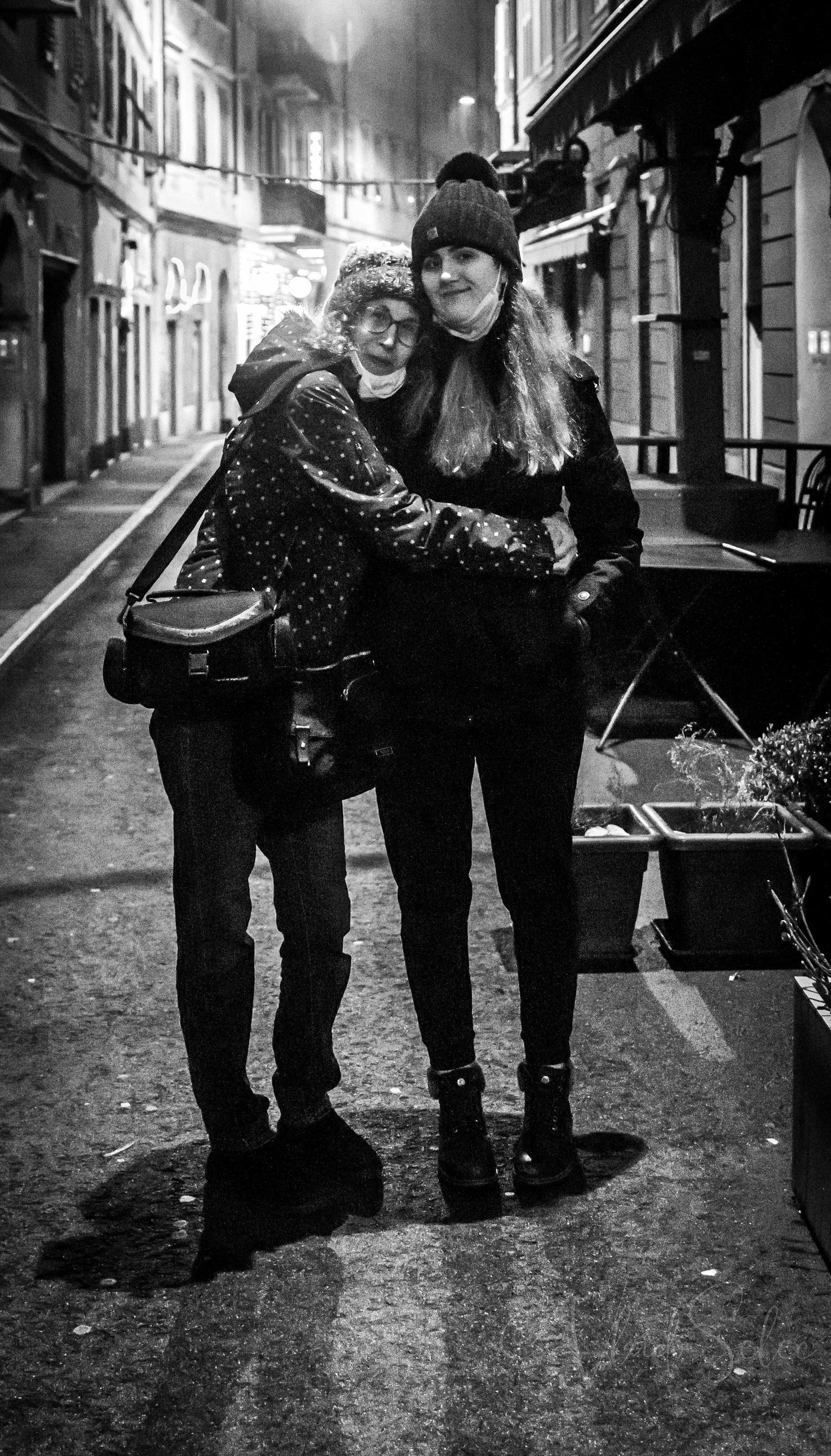 Two women hugging and smiling on a rainy night street in black and white urban photography.