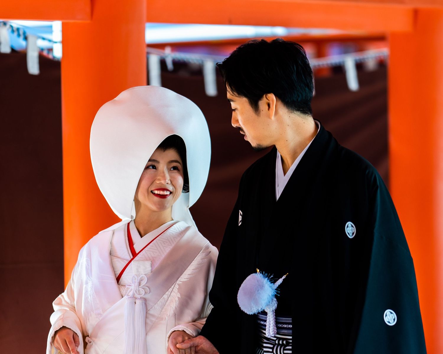 Couple in traditional Japanese wedding attire, bride in white kimono and tsunokakushi hat, groom in black hakama.