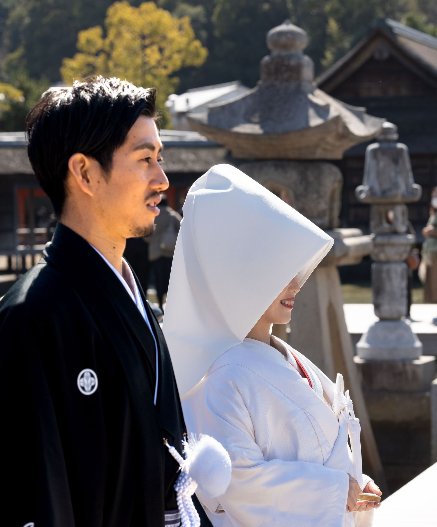 Japanese couple in traditional Shinto wedding attire walking through a historic shrine outdoors.
