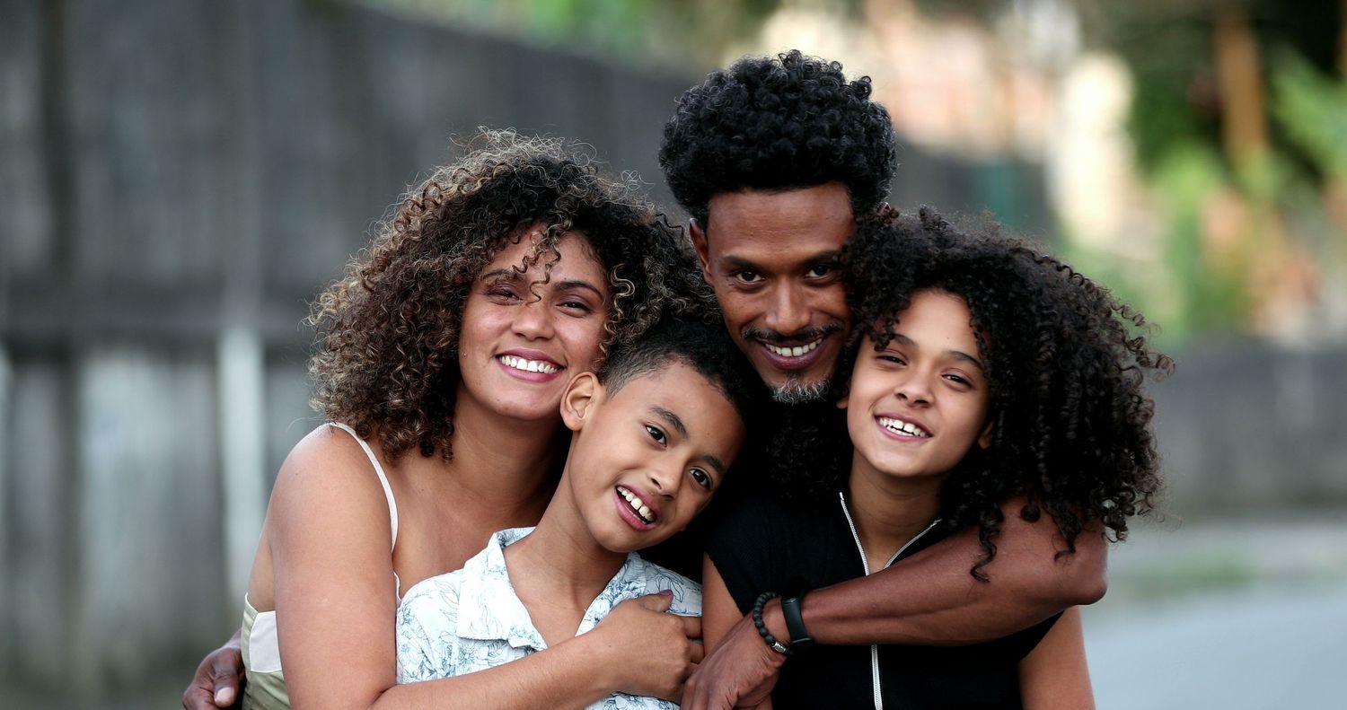 Happy Black family of four smiling and embracing outdoors, parents with two curly-haired daughters.