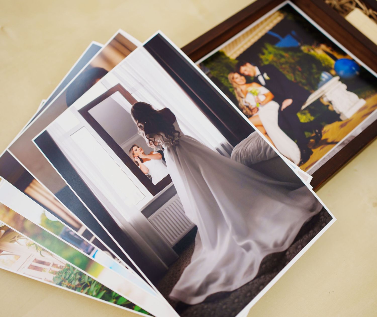 A collection of wedding photos spread on a table, featuring a bride in a flowing white gown near a window.
