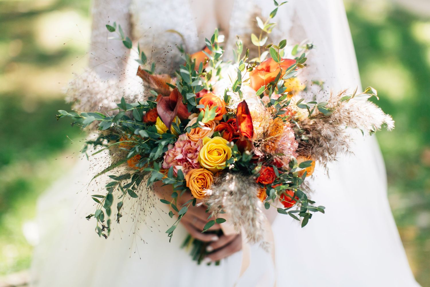 Bride holding a vibrant autumn wedding bouquet with orange roses, greenery, and dried flowers.