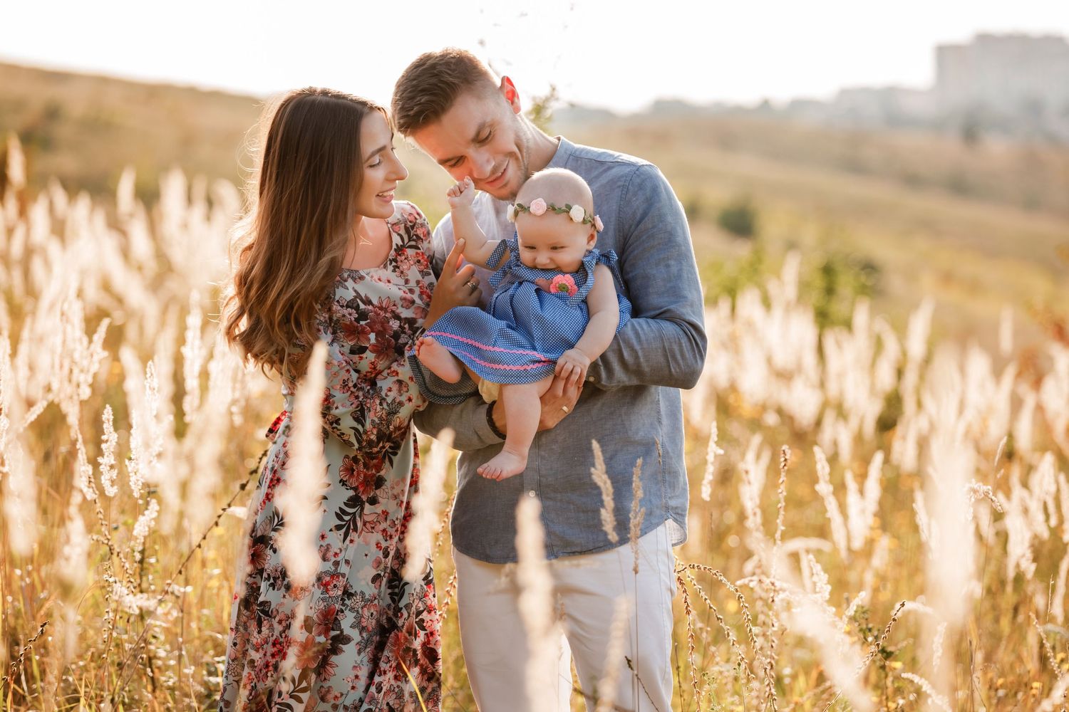 Happy young family with a baby standing in a golden sunlit field at sunset.