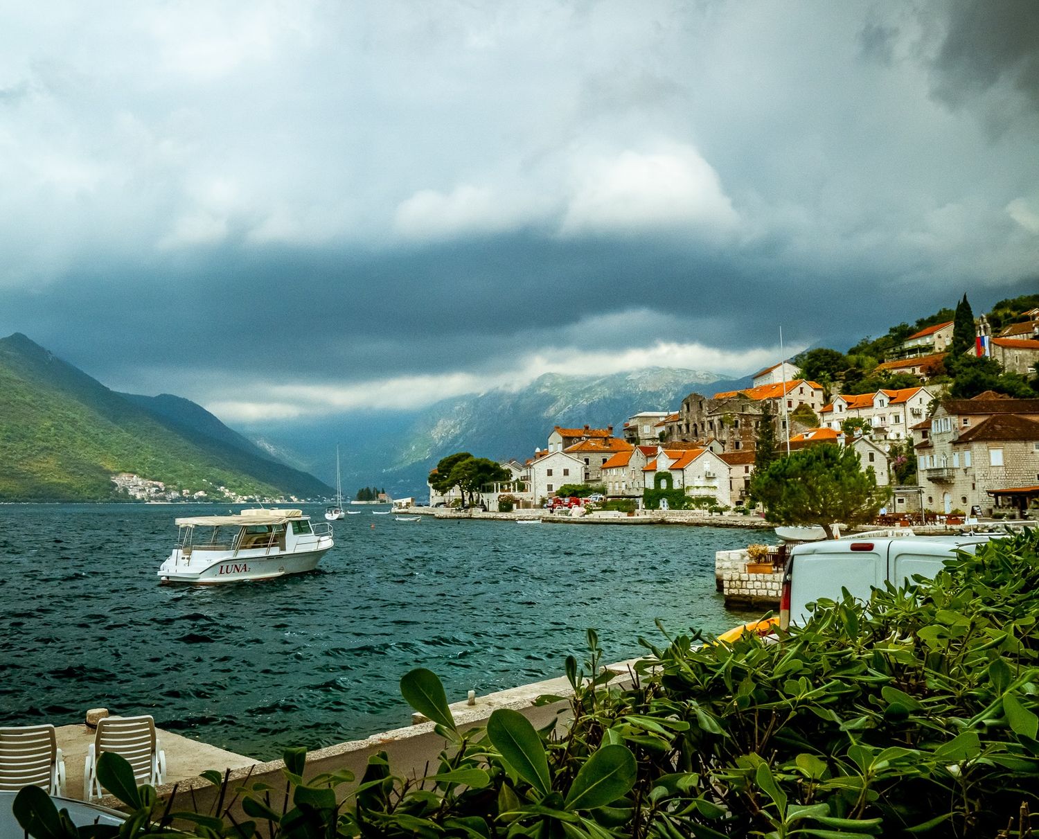 Scenic coastal village of Perast in Montenegro with boats on Bay of Kotor and dramatic stormy mountain backdrop.