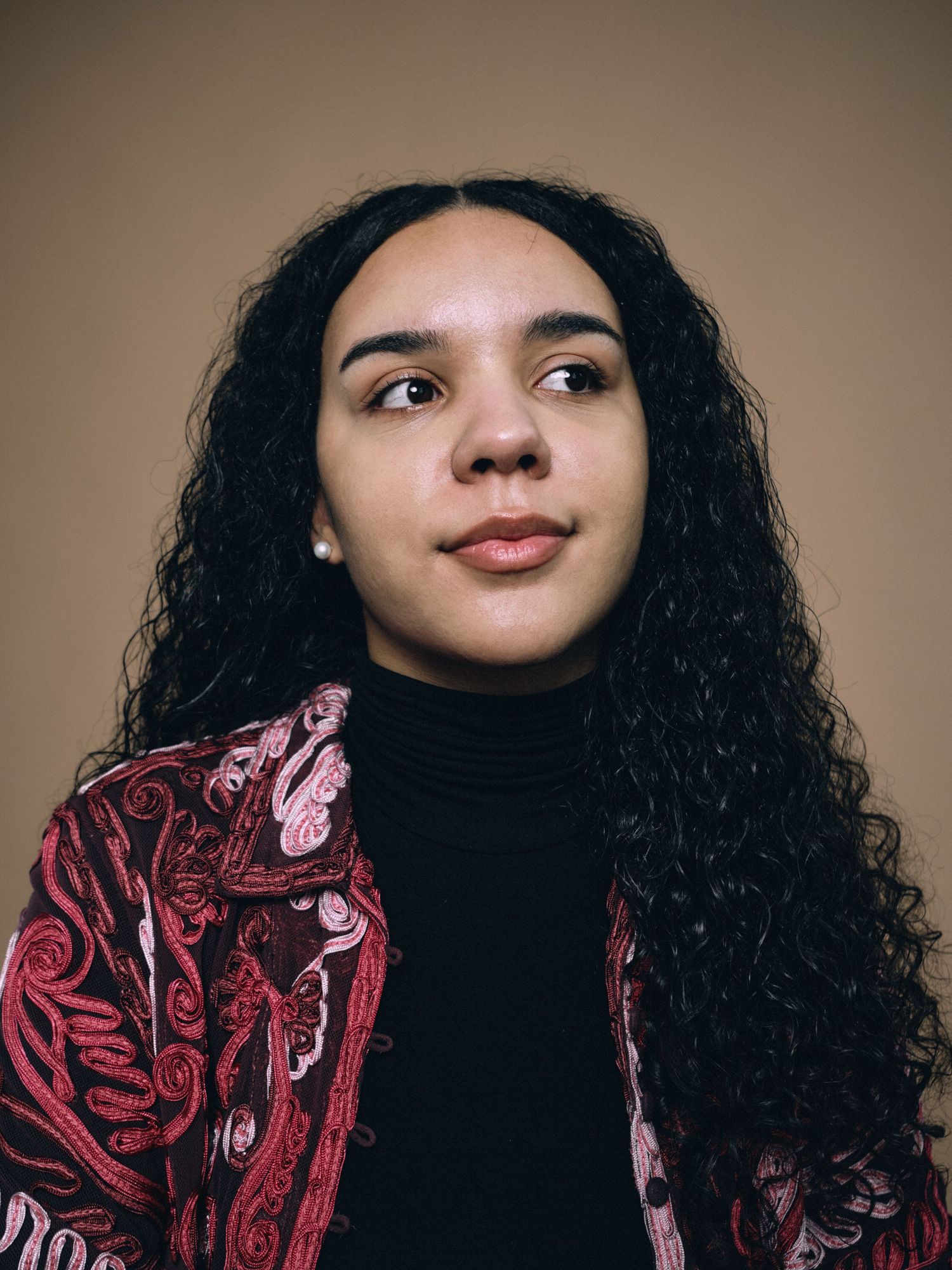 A head shot portrait of a woman in a pink shirt with brown curly hair