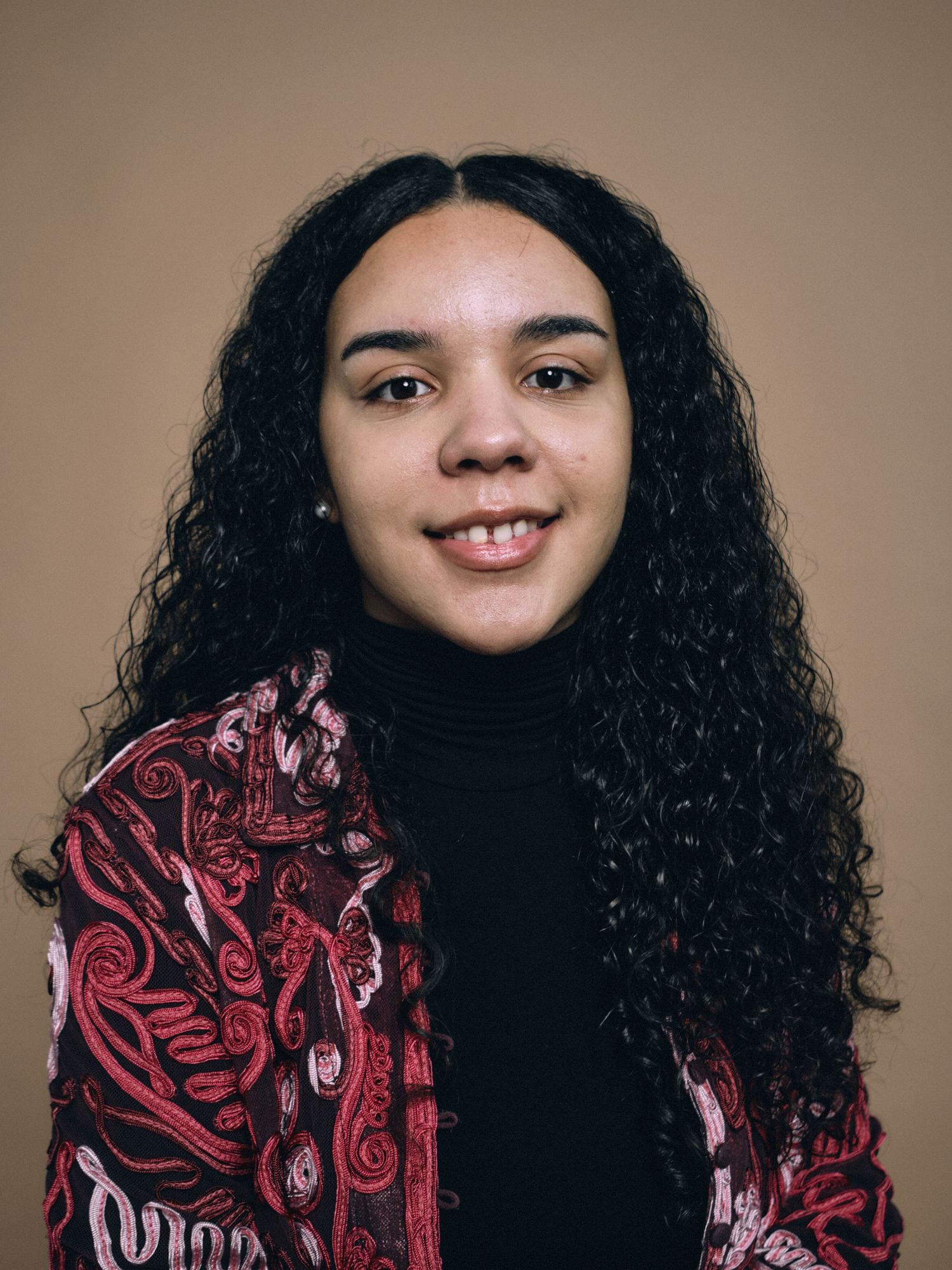 A head shot portrait of a woman in a pink shirt with brown curly hair
