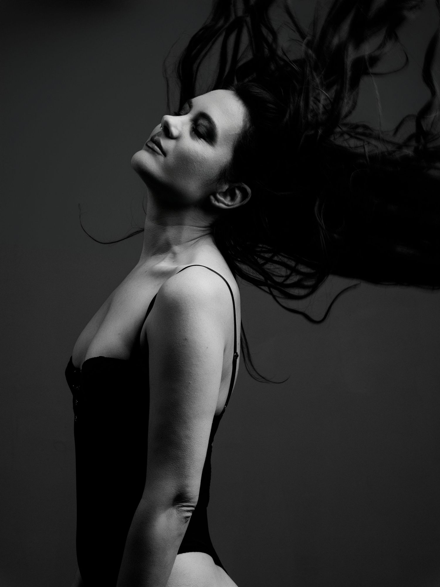 Black and white portrait of a woman in a bodysuit with hair flowing dramatically against a dark studio background.