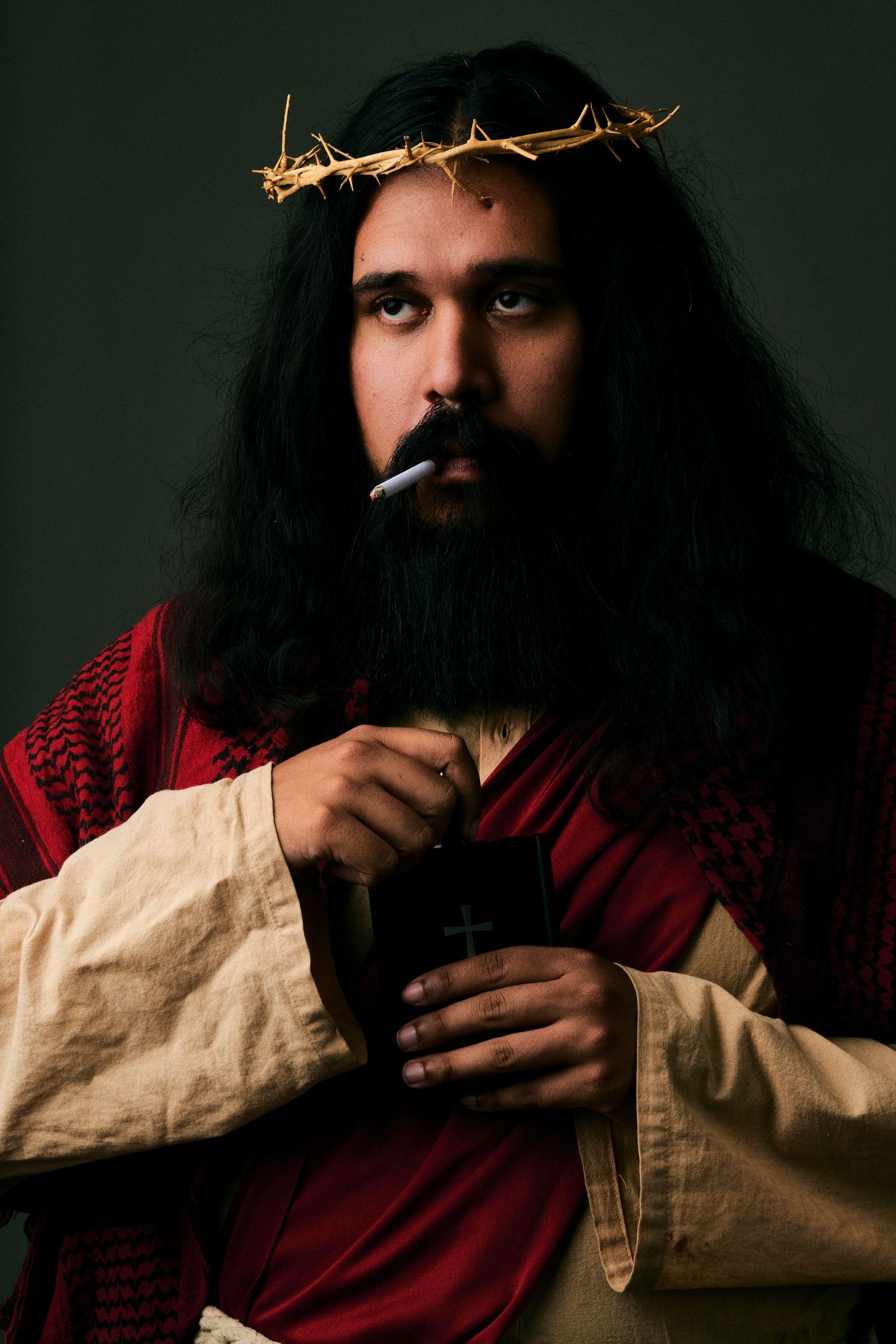 Man dressed as Jesus in crown of thorns and red robe, smoking a cigarette while holding a chalice.