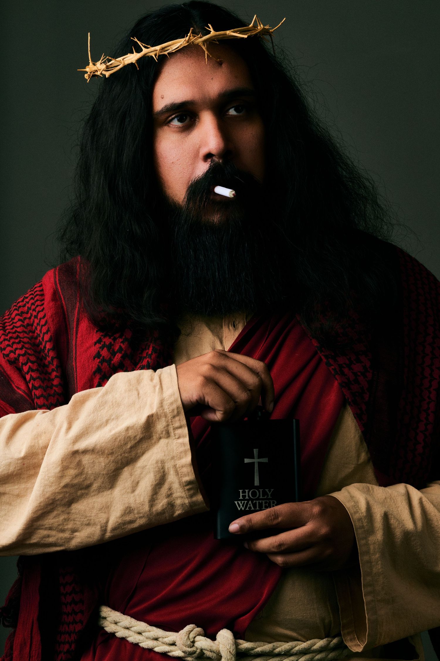 Man dressed as Jesus Christ holding Holy Bible, wearing crown of thorns and red robe, with rope around waist.