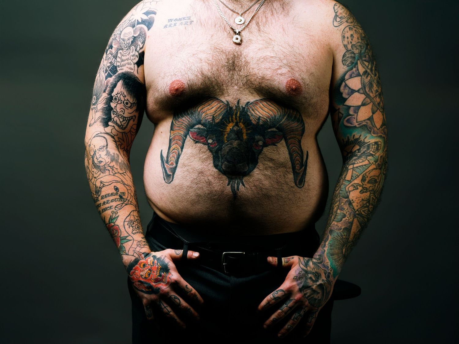 Shirtless tattooed man with full sleeve tattoos and a large bat chest tattoo, hands on hips.