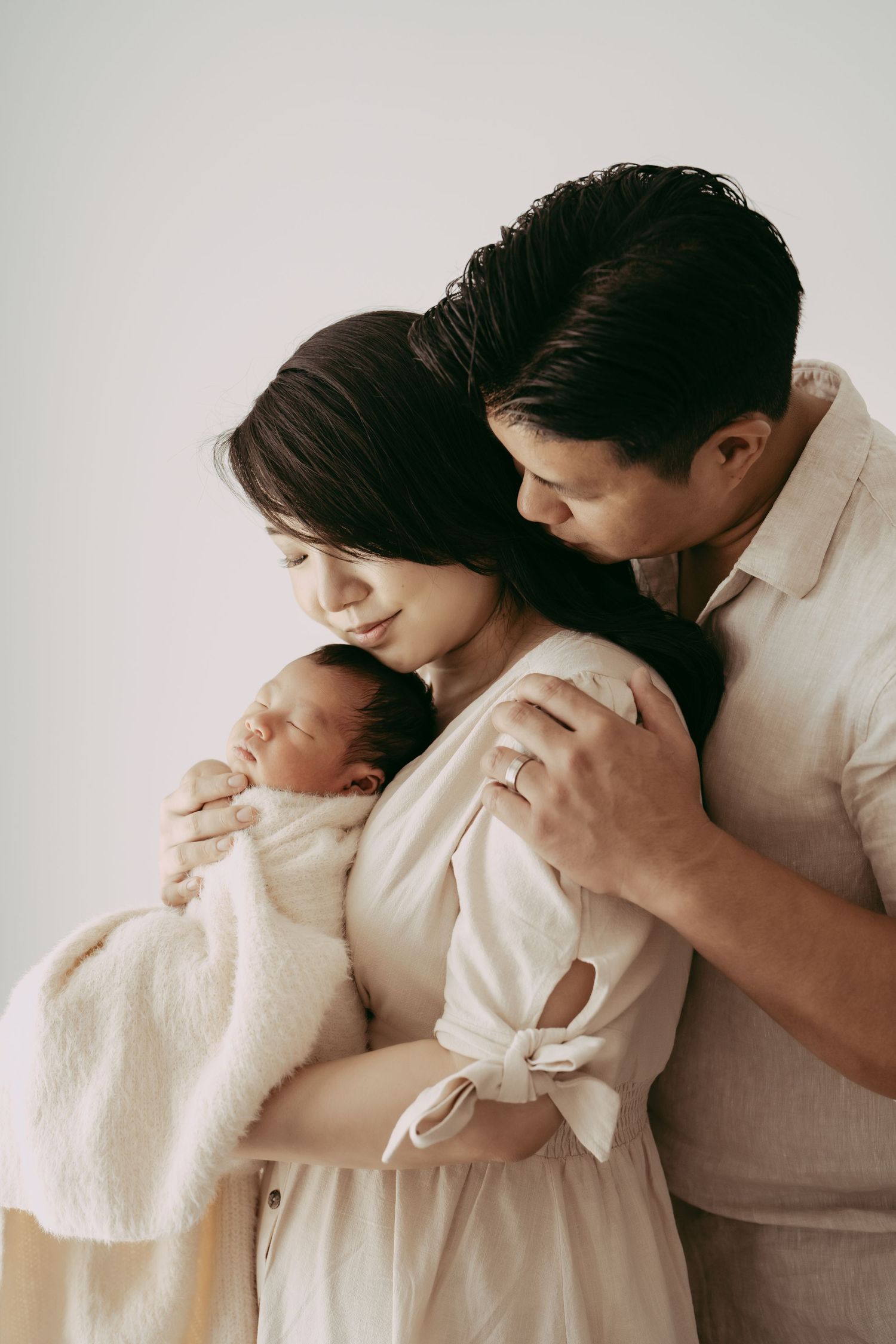 An intimate family moment with a newborn baby in gentle, minimalist studio lighting.