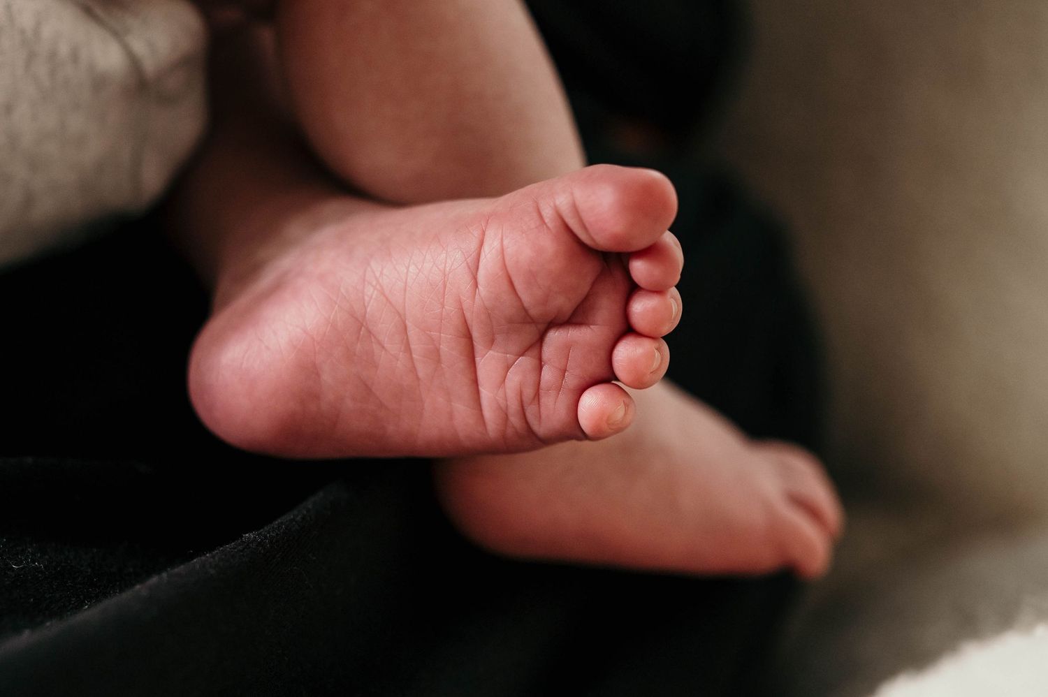 Close-up of a newborn baby's tiny bare foot with delicate toes resting on soft dark fabric.