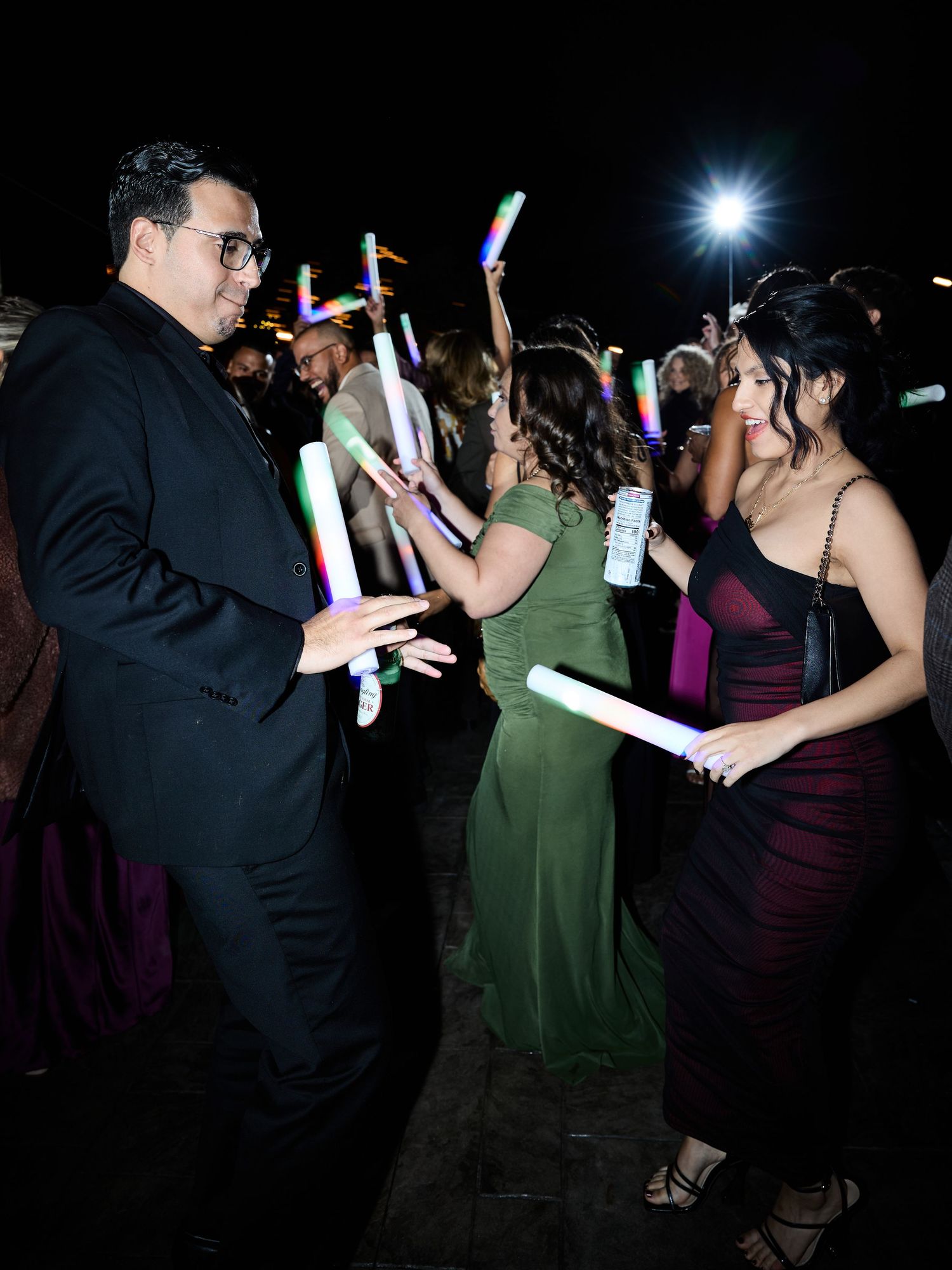 Wedding guests in formal attire dance with colorful glow sticks on the dance floor during a lively night reception.