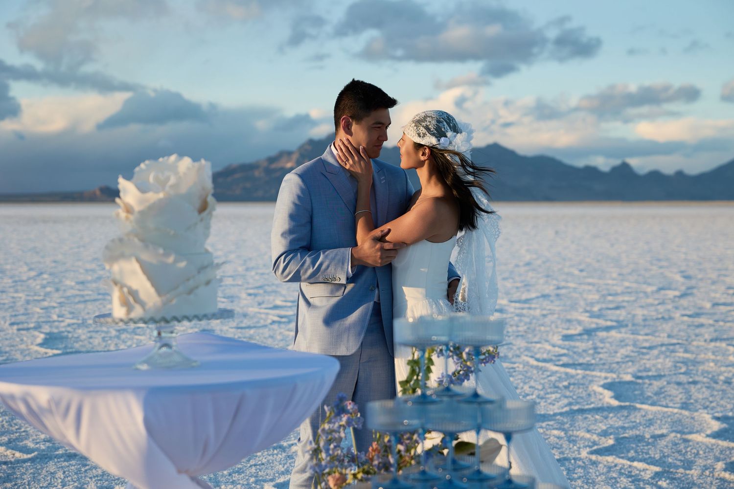 Groom gently touches his bride's face during a romantic salt flat wedding with a champagne tower and mountain backdrop.