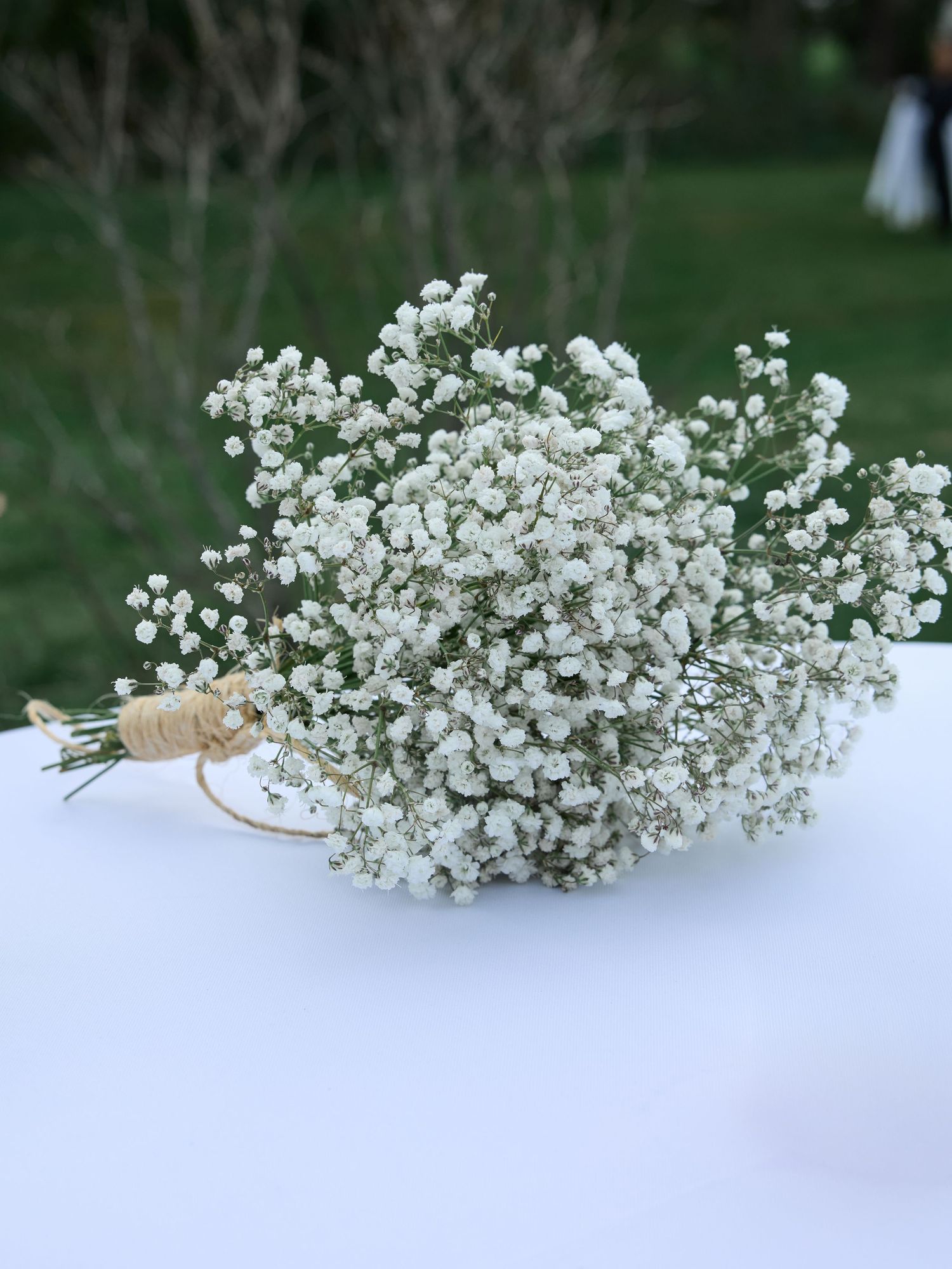Small baby's breath bridal bouquet tied with twine rests on a white table outdoors.