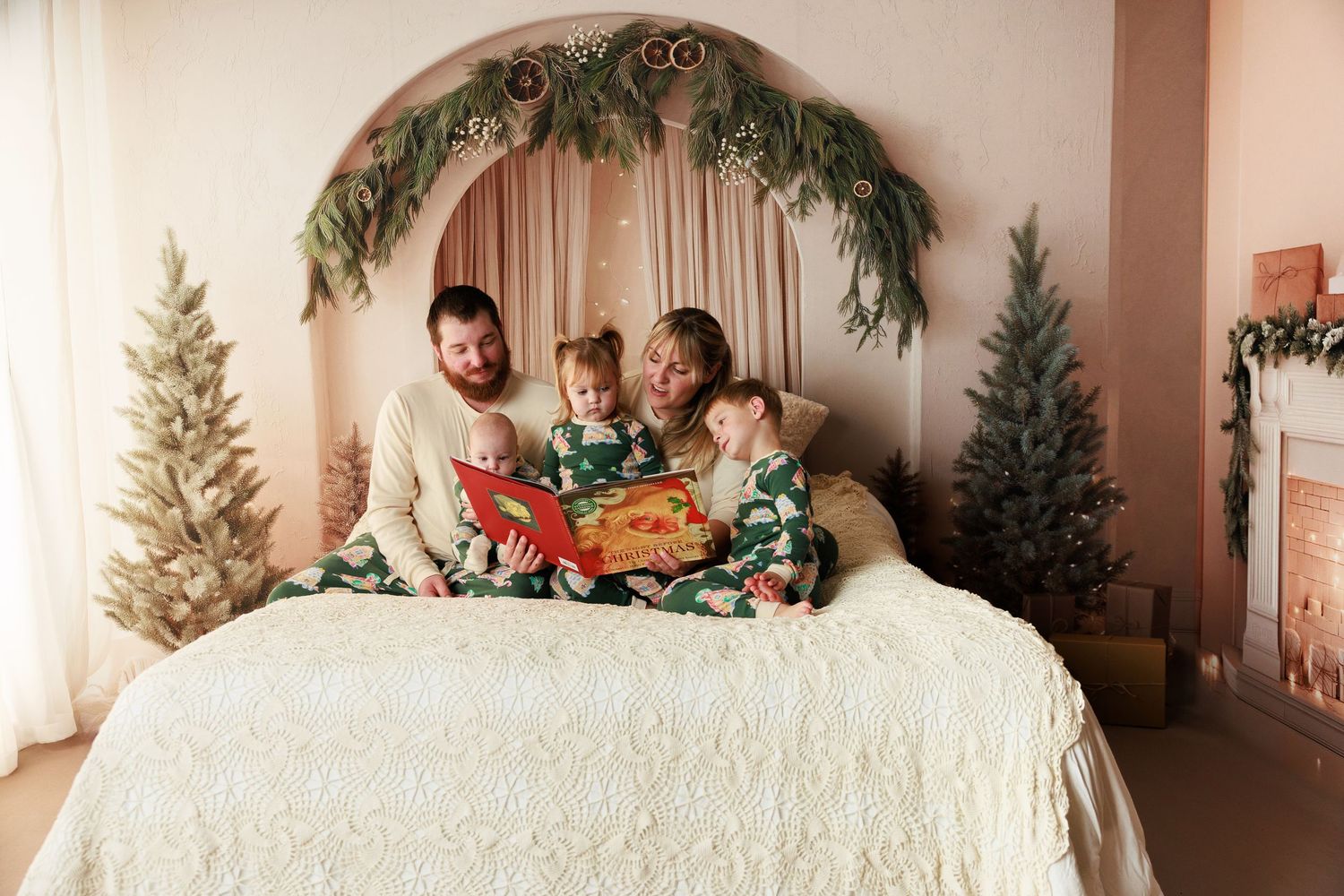 Family in matching Christmas pajamas reading a book together on a bed with festive holiday decor.