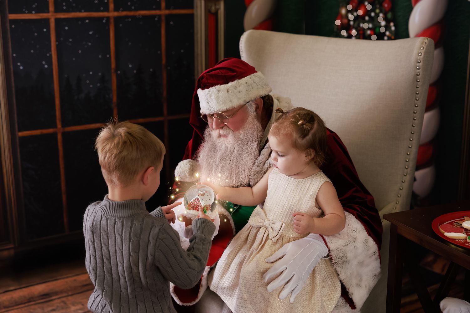 Two children visit Santa Claus, who sits in a chair holding a glowing sparkler during a festive Christmas photo session.
