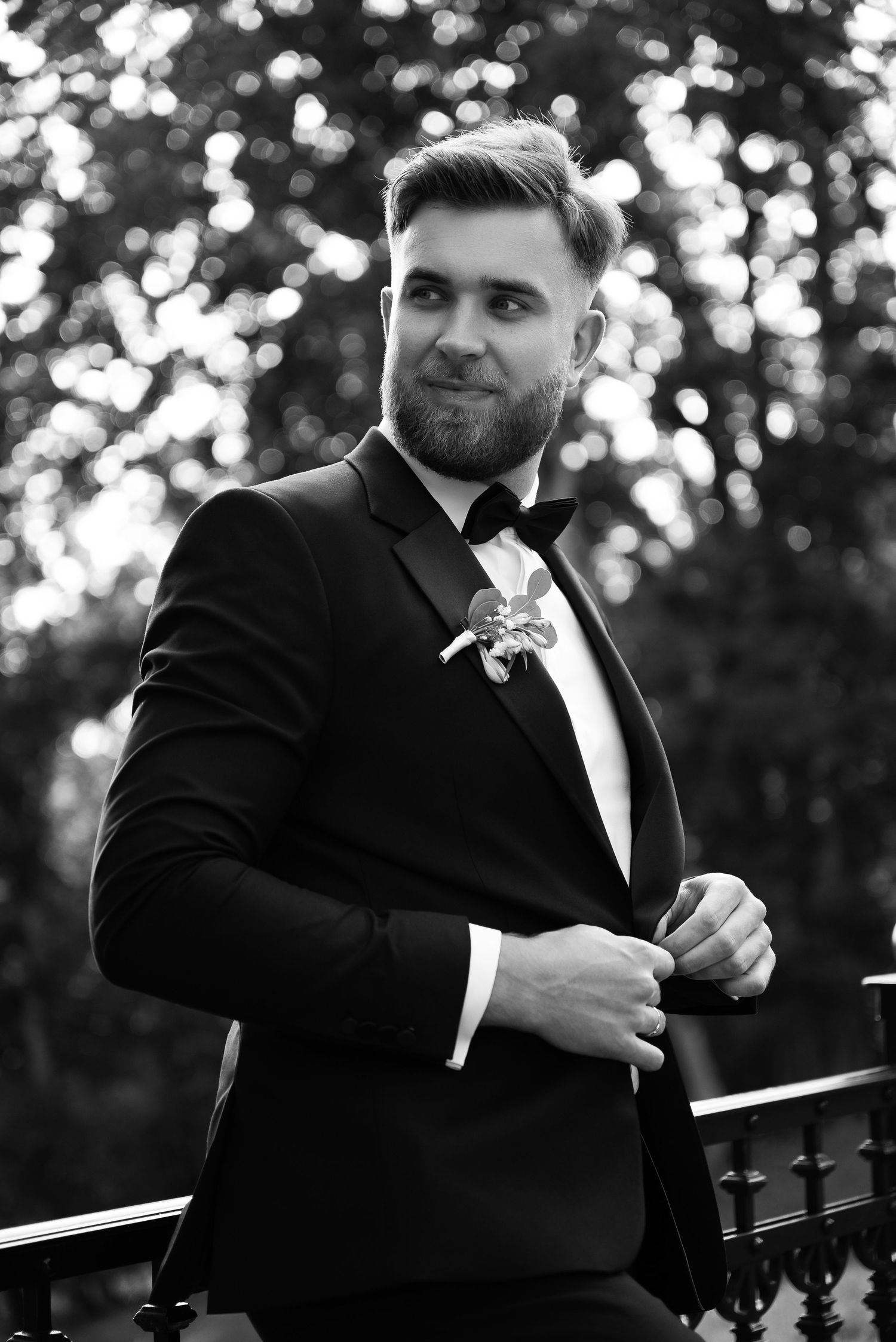 Black and white portraits of groom in tuxedo adjusting his bowtie.