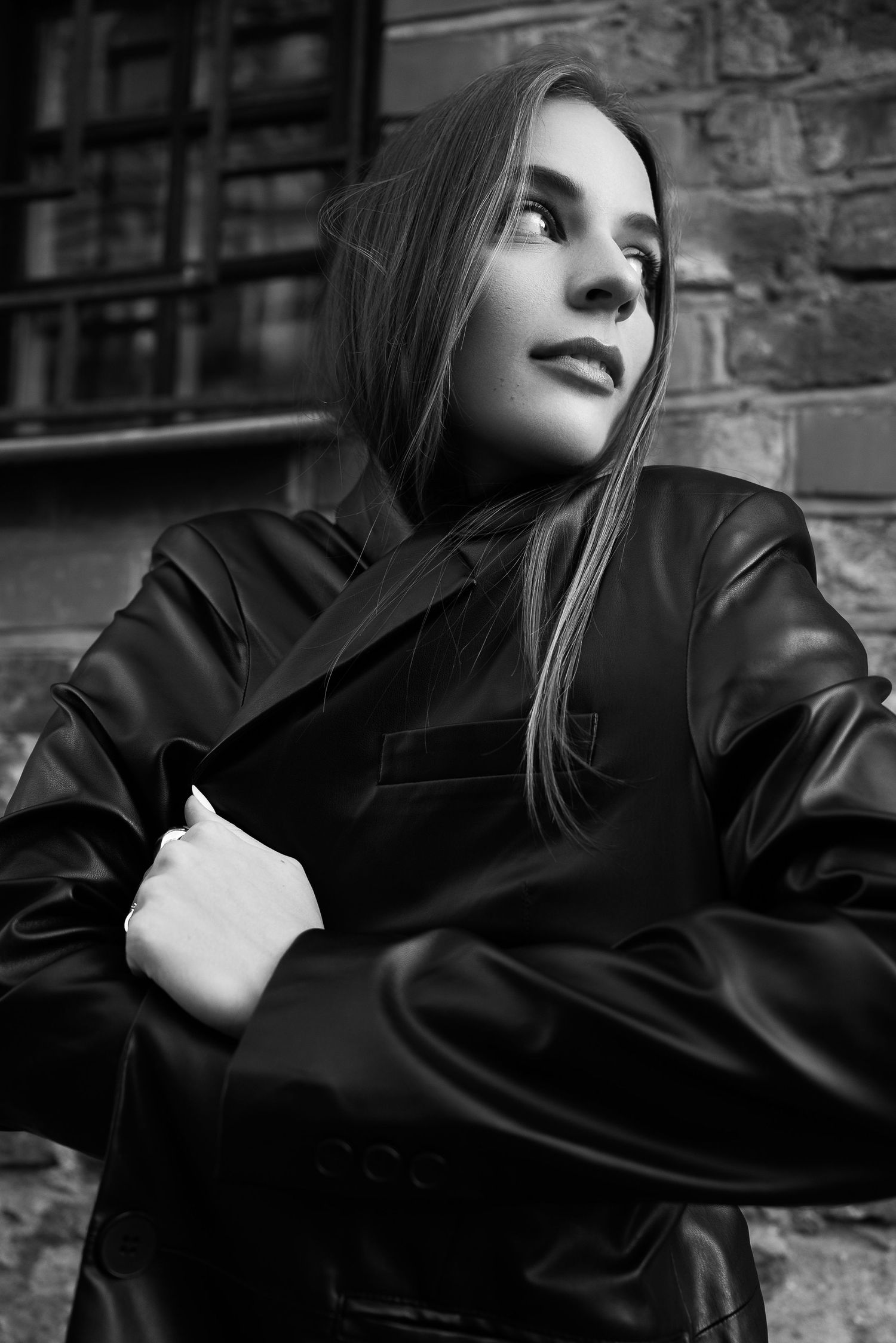 Moody black and white portraits against brick wall wearing leather jacket.