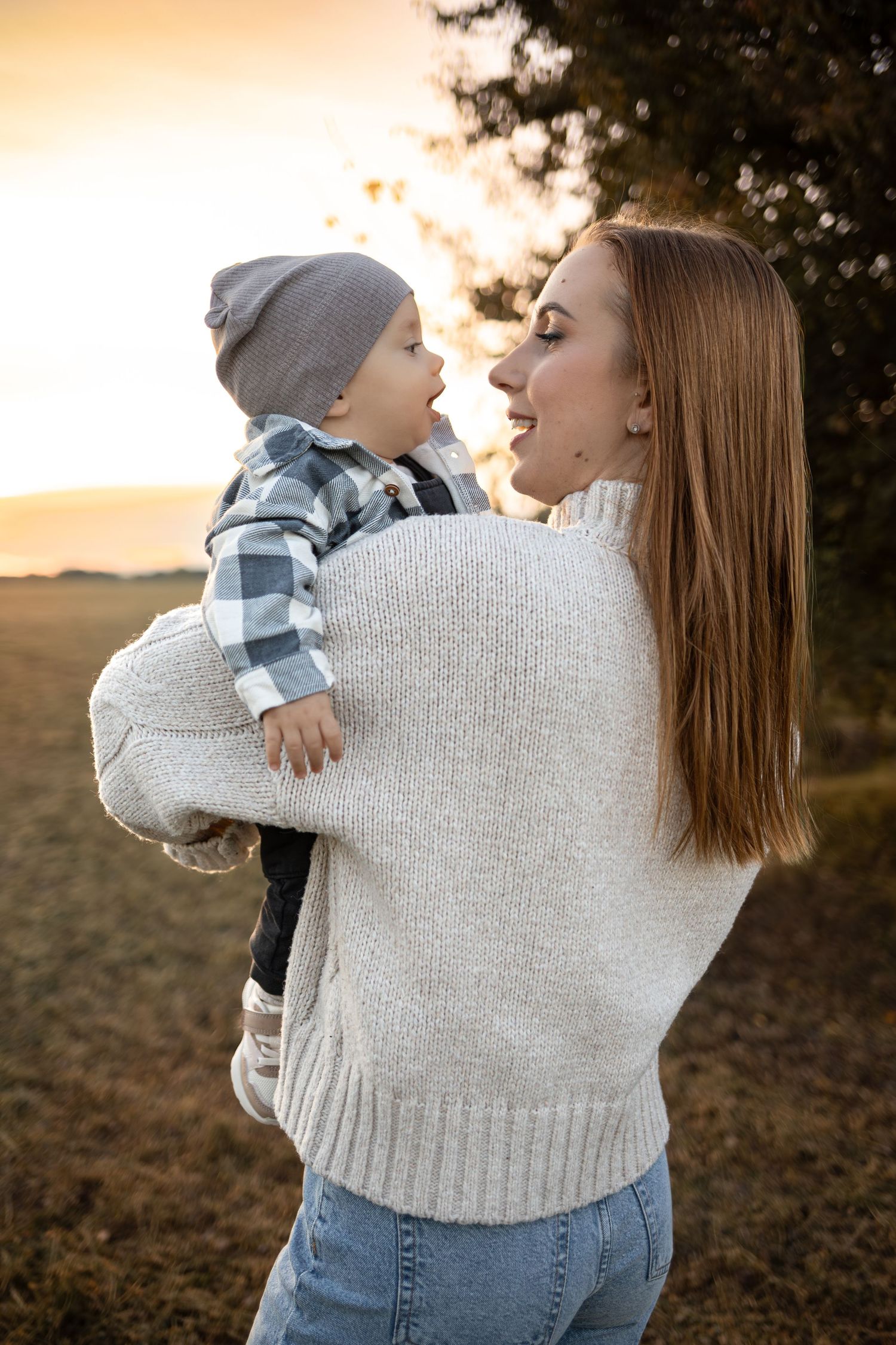 Mother and child sharing a tender moment at sunset in a cozy sweater and plaid outfit.