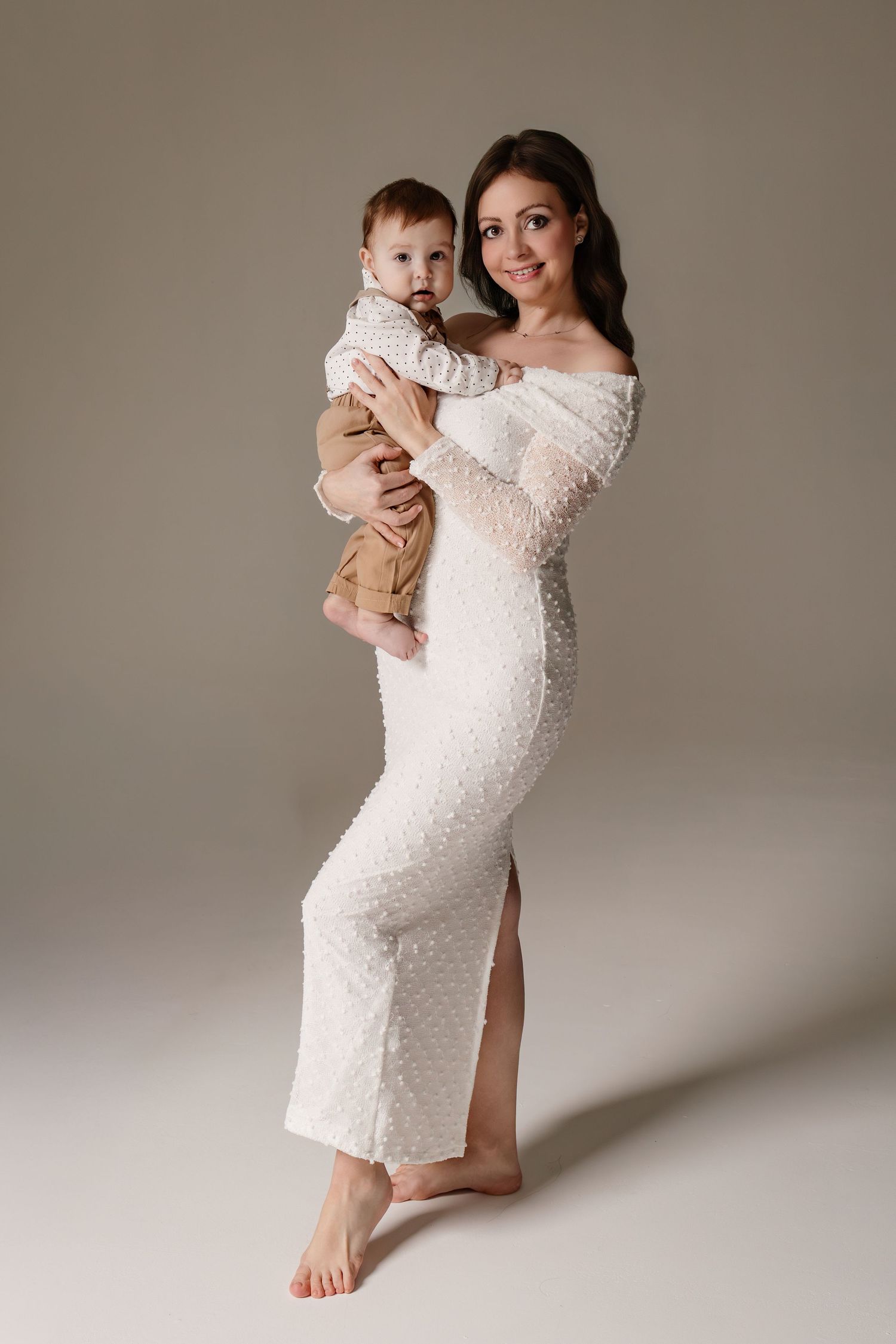 A maternity photo series showing a white lace dress against a neutral backdrop with elegant poses and a baby.