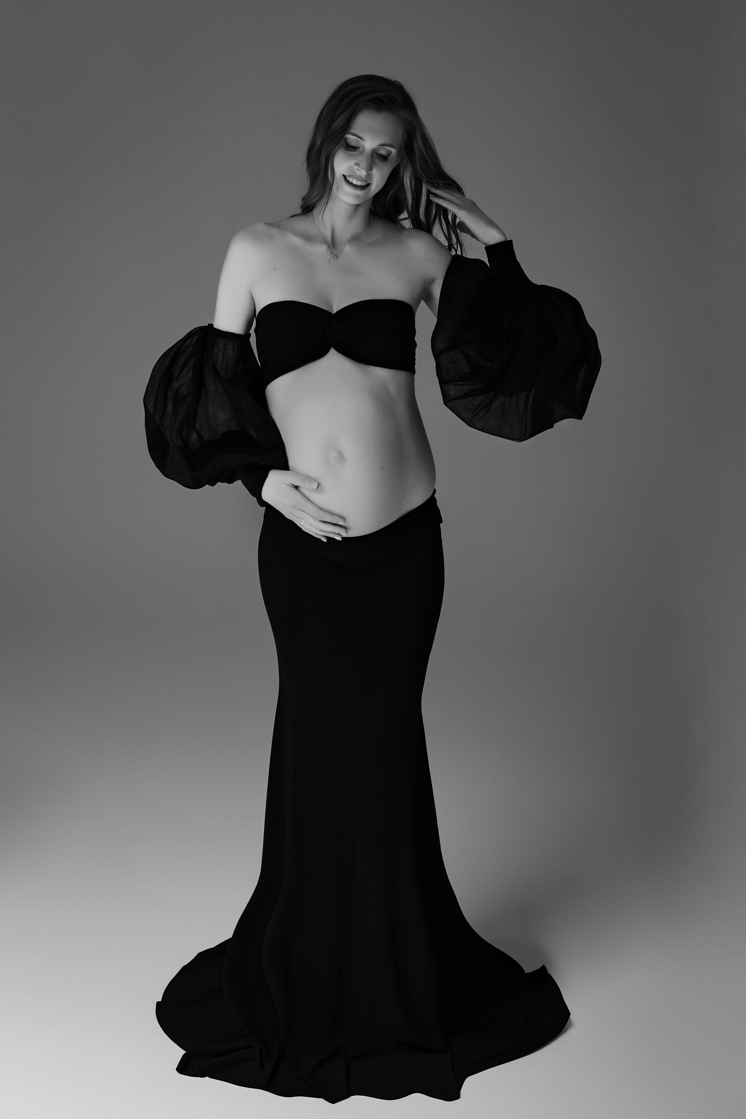 Black and white fashion photo showing a model in a dramatic floor-length skirt and cropped top with voluminous sleeves.