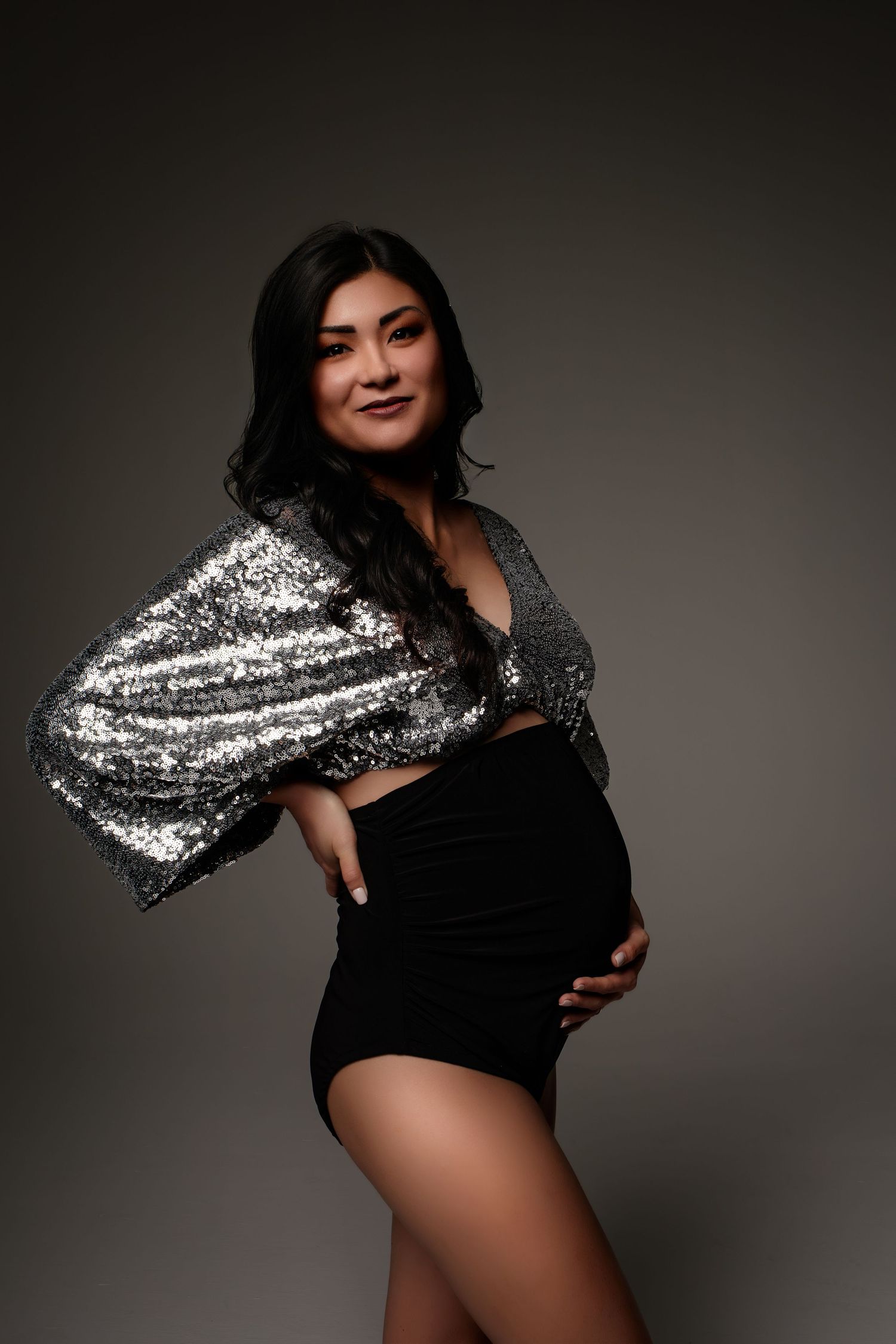 A maternity portrait features a sparkly silver sleeve and black bodysuit against a dark studio background.